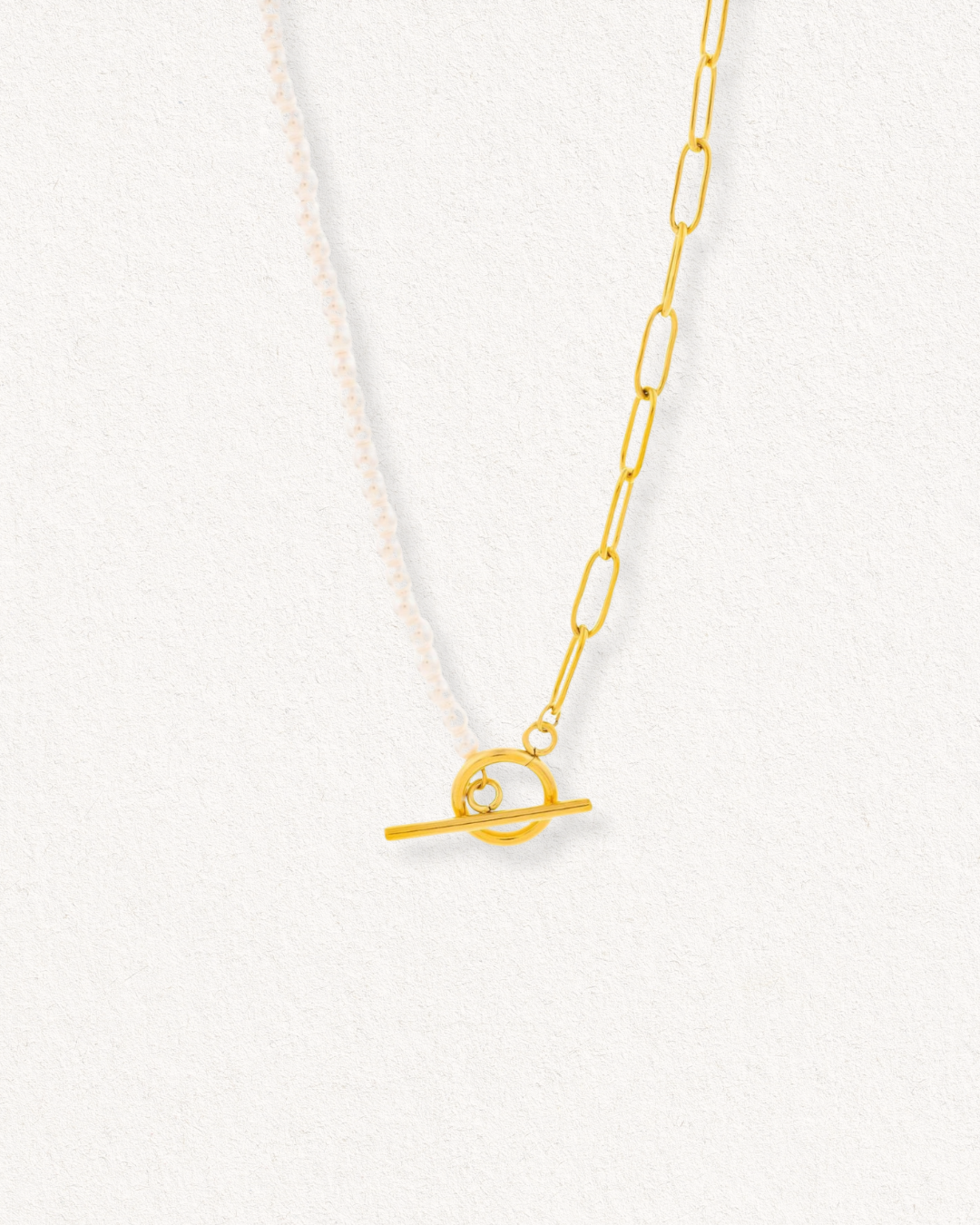 Como Jewelry Kaklarota - ar pērlēm ir divas pusītes: viena ar mazām baltām pērlēm, otra ar iegareniem zelta ķēdītes posmiem, kas savienoti ar zelta aizdares aizdari un izvietoti uz gaišas faktūras fona.