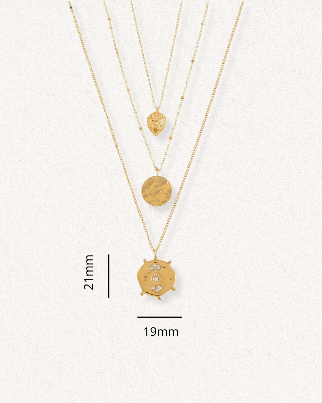 Trīs zelta piekariņu kaklarotas no Como Jewelry Kaklarotu komplekts Gaismas kārtas ir izkārtotas uz fakturēta balta fona. Šajā antialerģiska rotaslietā ir lielākais kulons, kura augstums ir 21 mm un platums - 19 mm, ar attēlotām mērījumu līnijām.