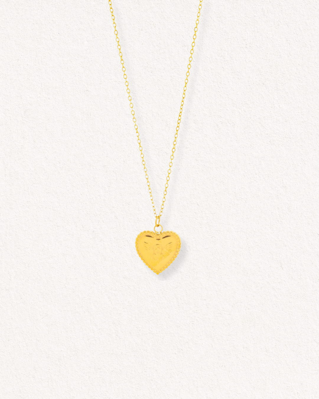 Kaklarota - Sirds by Como Jewelry ir maiga juveliertērauda kaklarota ar nelielu, teksturētu sirds formas piekariņu, kas izvietots uz gaiša, teksturēta fona.