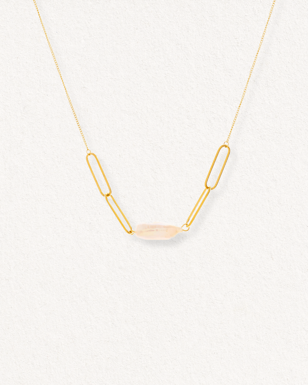 Kaklarota - Siltums no Como Jewelry ir ar trim garenām ķēdītes saitēm katrā pusē un centrālo ovālu, caurspīdīgu akmeni, kas izvietots uz gaišas faktūras fona.