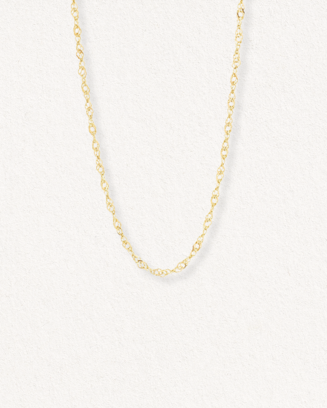 Kaklarota - Zelta vijums no Como Jewelry ir smalka vītā zelta virves ķēdīte uz gaiša fona - eleganta, antialerģiska rotaslieta, kas ideāli piemērota ikdienas valkāšanai.