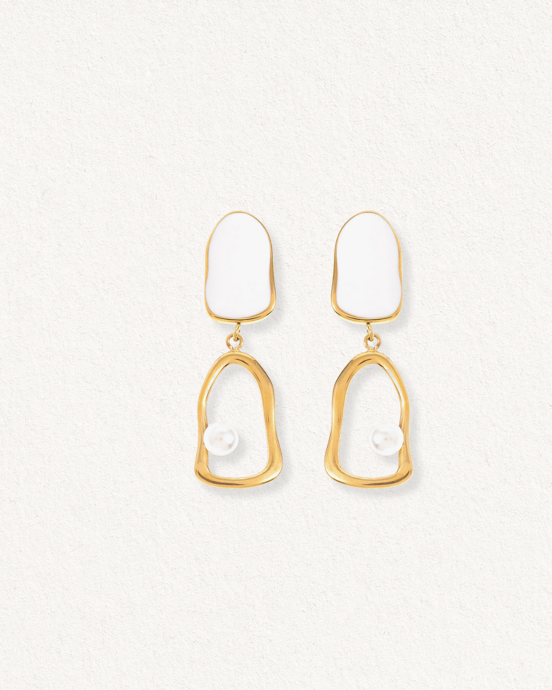 Auskari - Atspulgs are gold-plated drop earrings with irregular oval shapes, showcasing a white enamel top and a single small pearl accent inside each lower open frame, set against a light textured background.