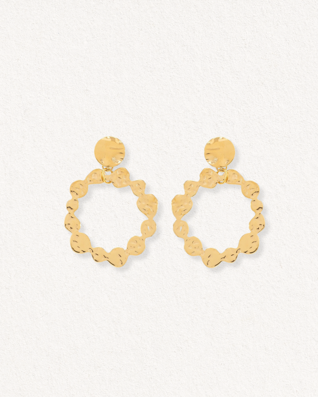 Auskari - Saules Rats no Como Jewelry - ar zelta pārklājumu, viļņveida tekstūru un atvērtu apaļu dizainu, eleganti izcelti uz gaiša fakturēta fona.