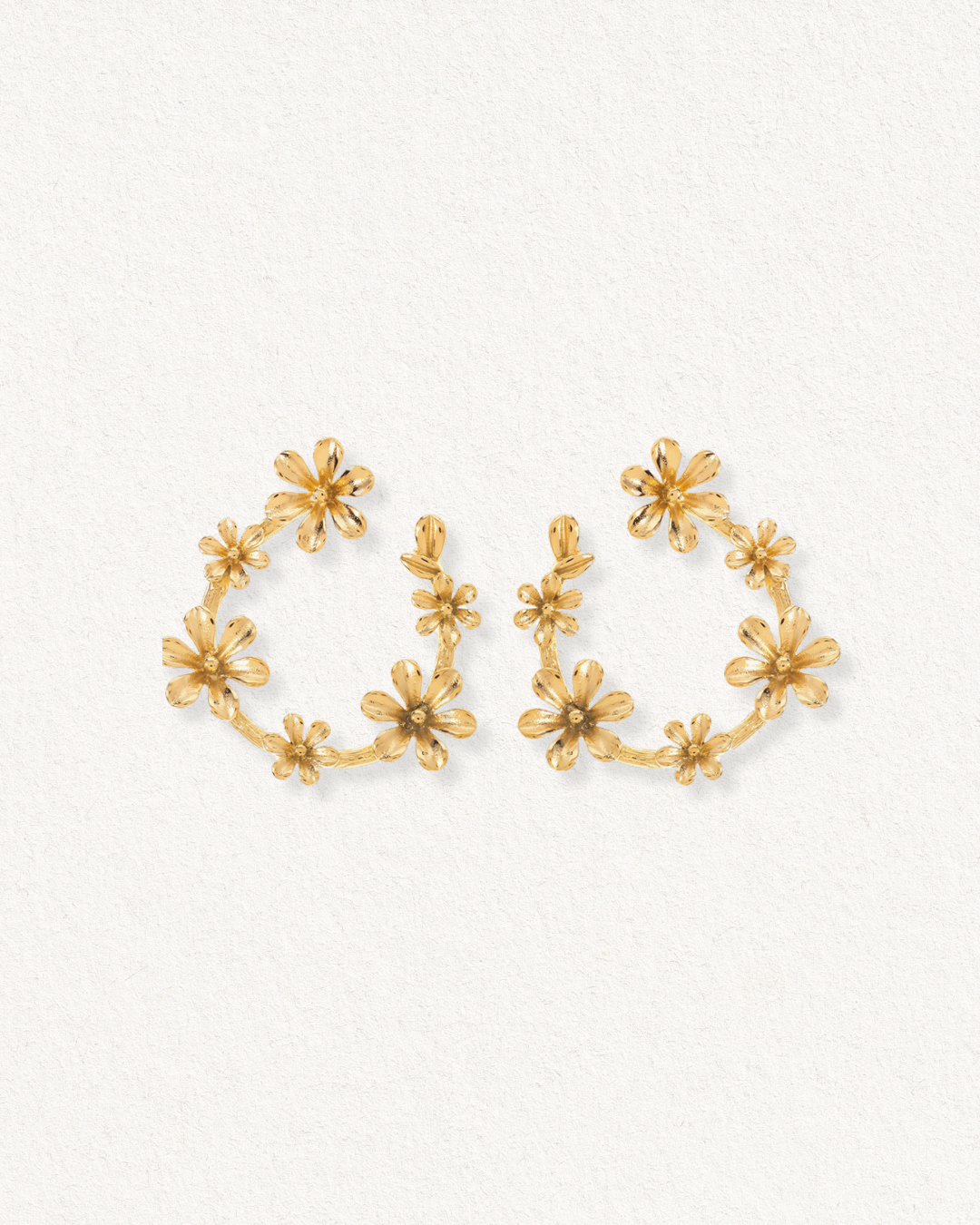 Como Jewelry Auskari - Rokoko: zelta riņķveida auskari ar zelta pārklājumu, rotāti ar vairākiem smalkiem ziediem gar riņķi, kas izvietoti uz gaišas faktūras fona.