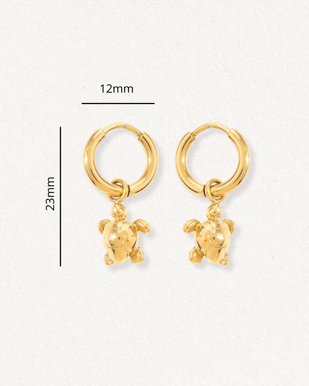 Auskari - Miers: juveliertērauda zeltīti stīpu auskari (12mm) ar bruņurupuču piekariņiem (kopgarums 23mm), izvietoti uz gaiša fona.