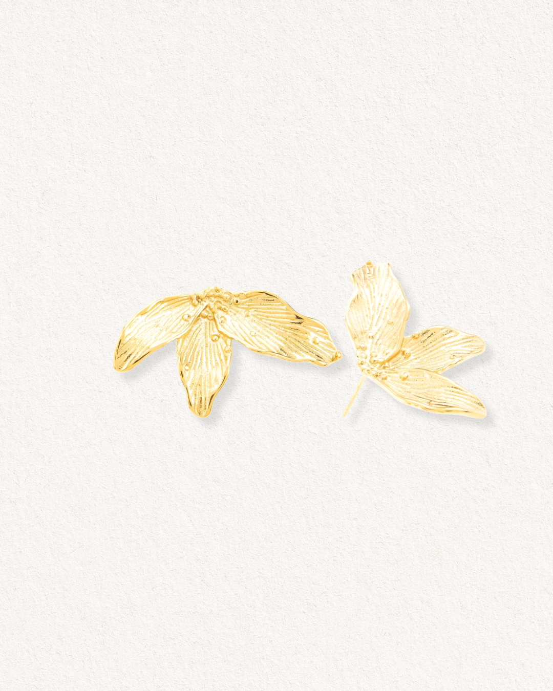 Como Jewelry Mazie auskari - Ziedlapiņas: zelta pārklāts nerūsējošais tērauds, kas veidots no zelta pārklājuma, uz gaiša, neitrāla fona, un tam ir zelta toņa lapu formas auskari.