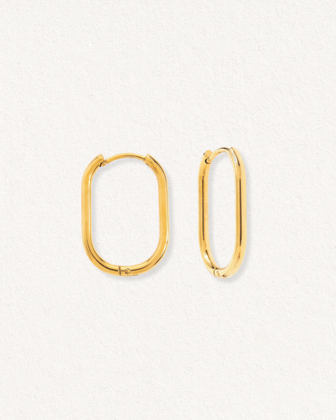 Mazie auskari - Ovāls by Como Jewelry: iegareni, noapaļoti taisnstūra formas auskari ar elegantiem zelta pārklājumiem, kas izvietoti uz fakturēta, baltas krāsas fona. Viens auskars vērsts uz priekšu, otrs ir redzams no sāniem.