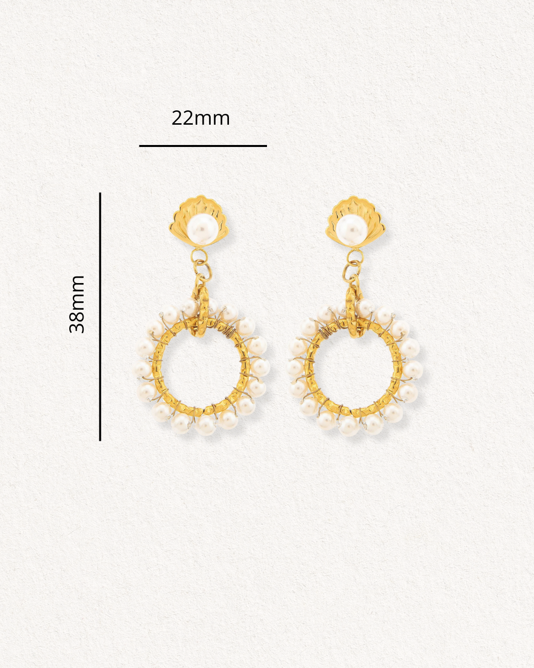 Como Jewelry Mazie auskari - Pērļu dārzs: zelta krāsas nerūsējošā tērauda auskari ar perlamutra pērļu rotājumu loku malās, robotu dizaina nags. Izmēri: 38 mm garš, 22 mm plats. Prezentēti uz gaiša teksturēta fona.