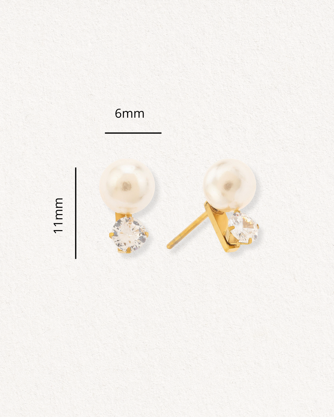 Como Jewelry Mazie auskari - Klusā gaisma ir minimālisma stila zeltīti auskari ar apaļām pērlēm un caurspīdīgiem dārgakmeņiem, hipoalerģiski, ar izmēriem 6 mm x 11 mm, uz gaišas faktūras fona.