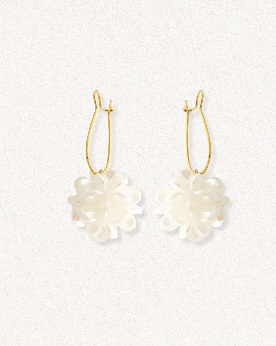 Auskari - Rītausma by Como Jewelry: elegantas ziedu formas baltas piekariņu cilpas sievietēm, kas skaisti izvietotas uz viegla faktūras fona.