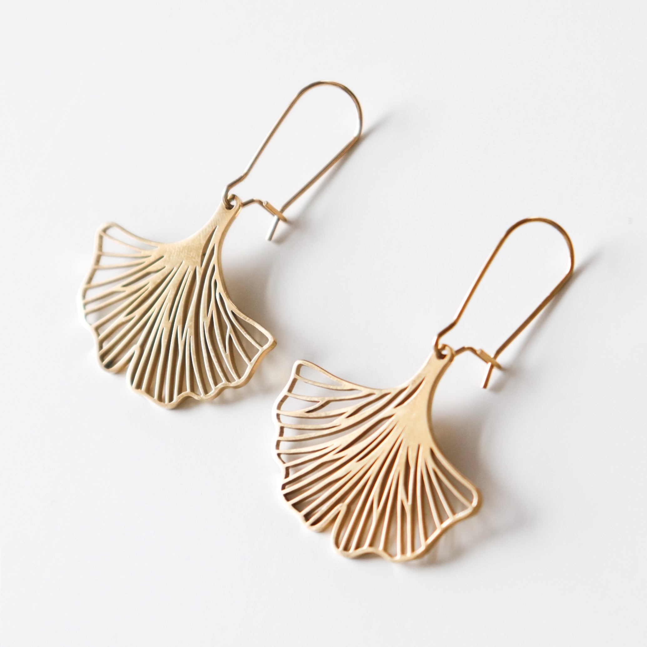 Auskari - Ginkgo: A pair of gold earrings inspired by ginkgo leaves, featuring delicate, intricate cut-out designs and displayed on a plain white background.