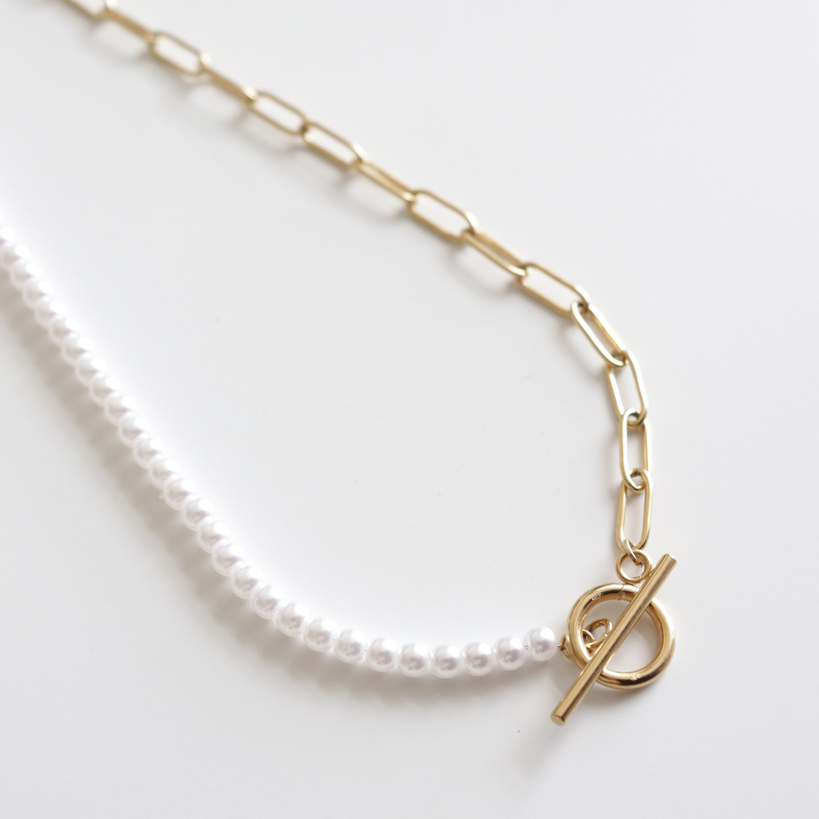 Kaklarota - ar pērlēm no Como Jewelry: mūsdienīga kaklarota ar pusi baltām pērlēm, pusi zelta ķēdi un zelta aizdari, izcelta uz balta fona.