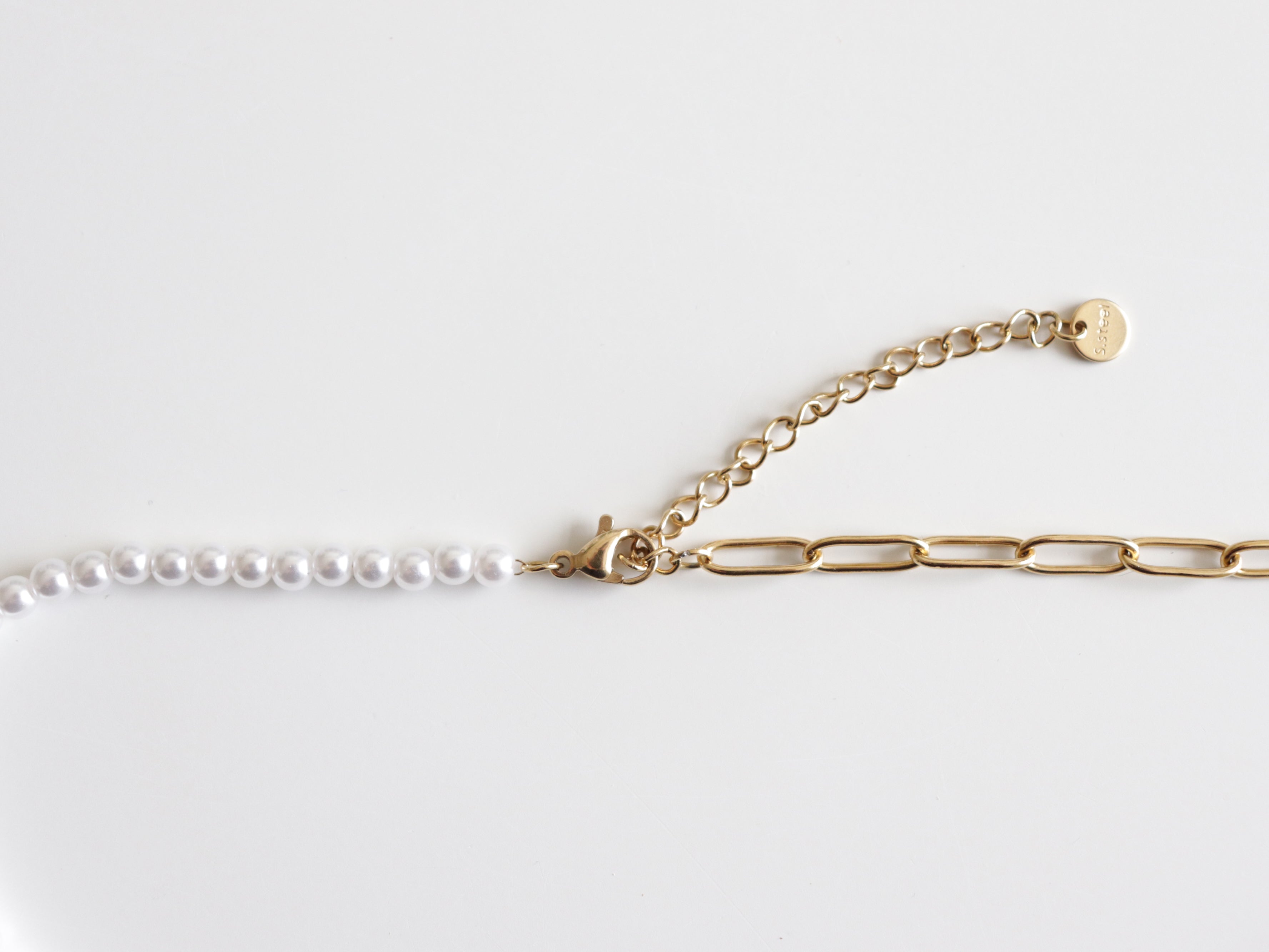 Mūsdienīgs Kaklarota - ar pērlēm no Como Jewelry: vienā pusē ir mazas baltas pērles, otrā - lieli zelta ķēdes posmi, savienoti ar zelta aizdares un regulējamu ķēdīti ar apaļu birku. Perfekta Zelta kaklarota sievietēm uz balta fona.