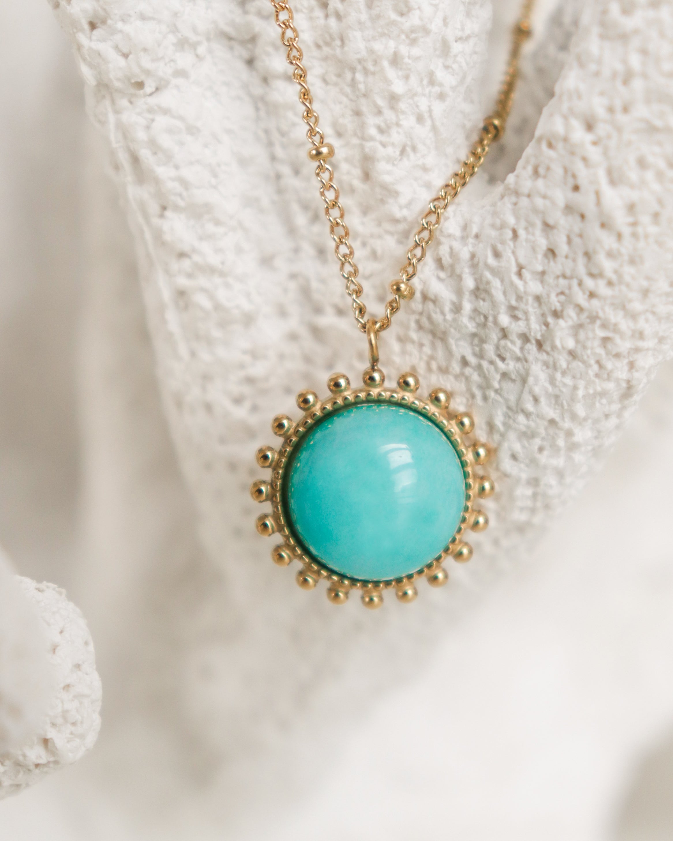 Kaklarota - Saules akmens by Como Jewelry ir juveliertērauda kaklarota ar zelta apaļu tirkīza piekariņu un pērlīšu apmali, kas attēlota uz balta fona.