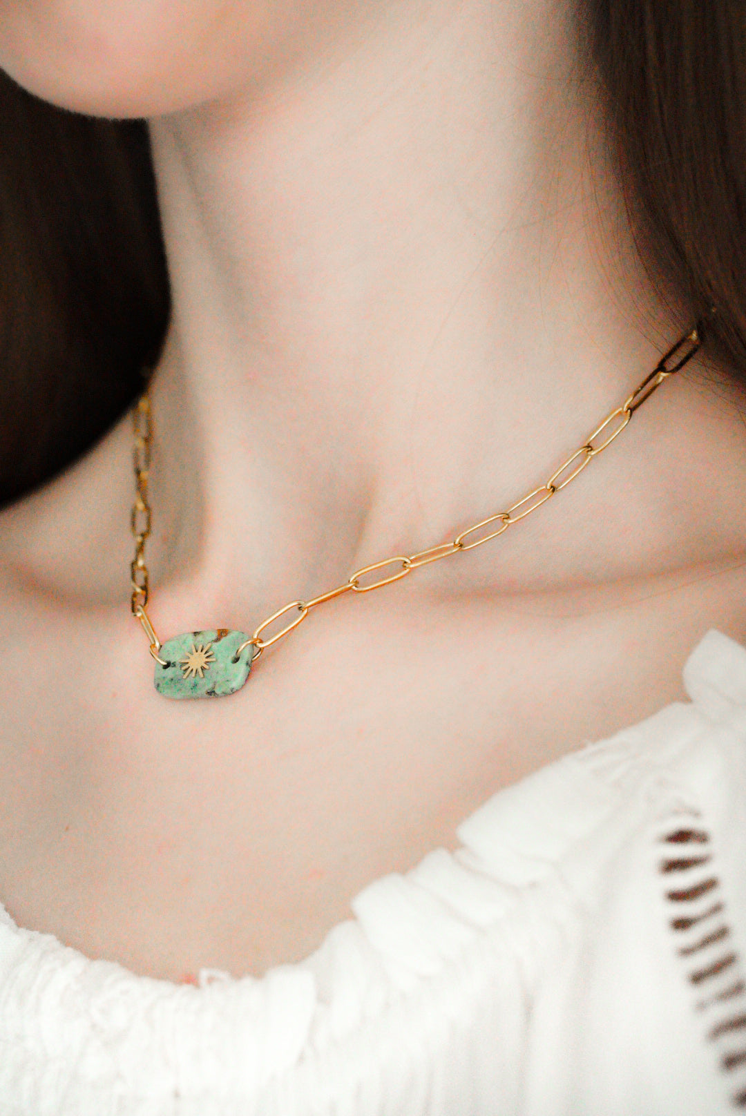 Tuvplāns sievietei, kurai mugurā ir Como Jewelry Kaklarota - Saules akmens ceļš ar zaļu un zelta krāsas taisnstūra formas piekariņu, kas kombinēts ar baltu fakturētu topu bez plecu apakšas. Šis ūdensizturīga kaklarota piešķir eleganci jebkuram tēlam.