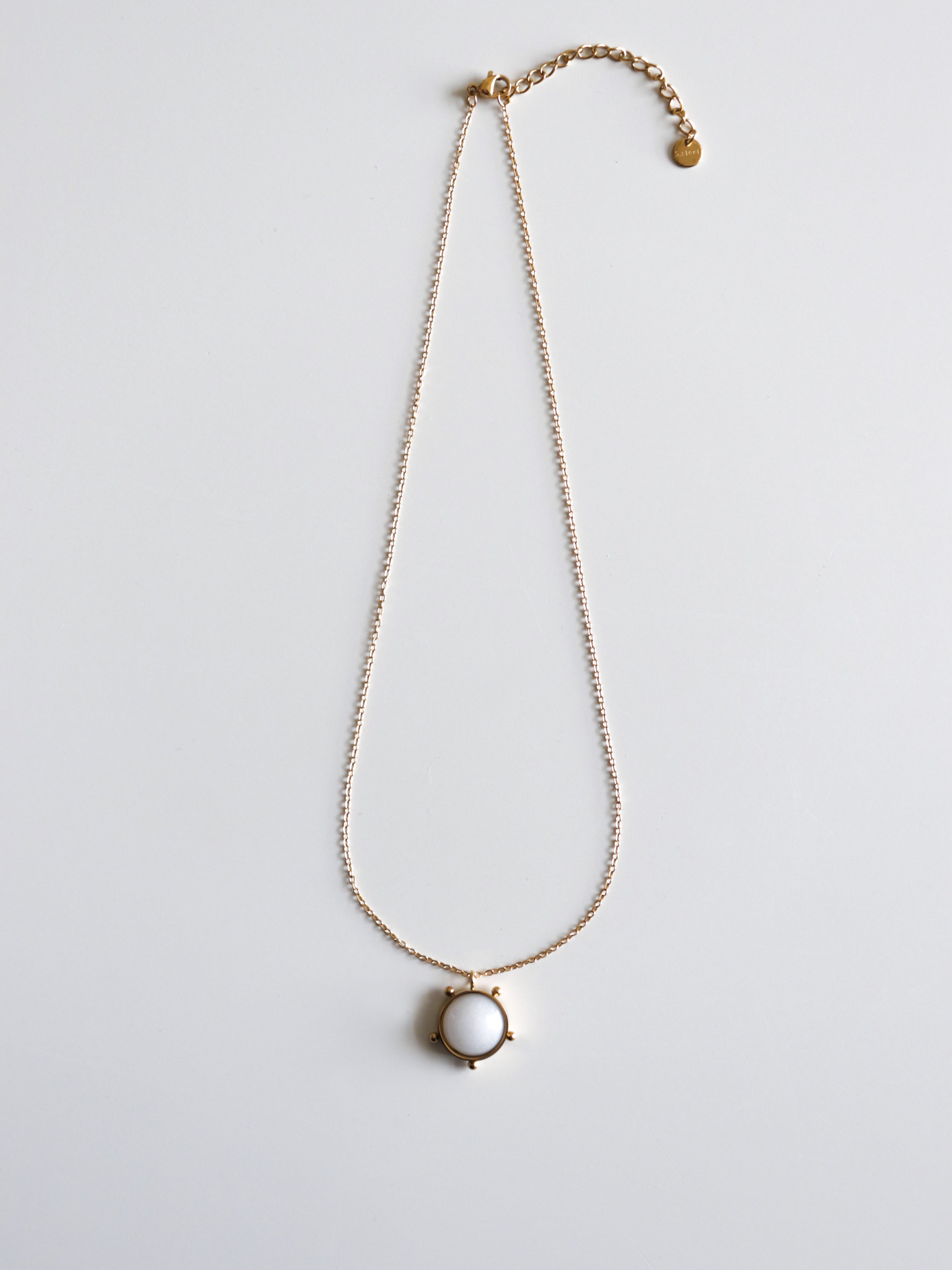 Kaklarota - Mēness gaisma by Como Jewelry ir smalka sieviešu kaklarota ar regulējamu aizdares aizdari un apaļu baltu piekariņu vienkāršā zelta ietvarā, kas attēlots uz vienkārša balta fona.