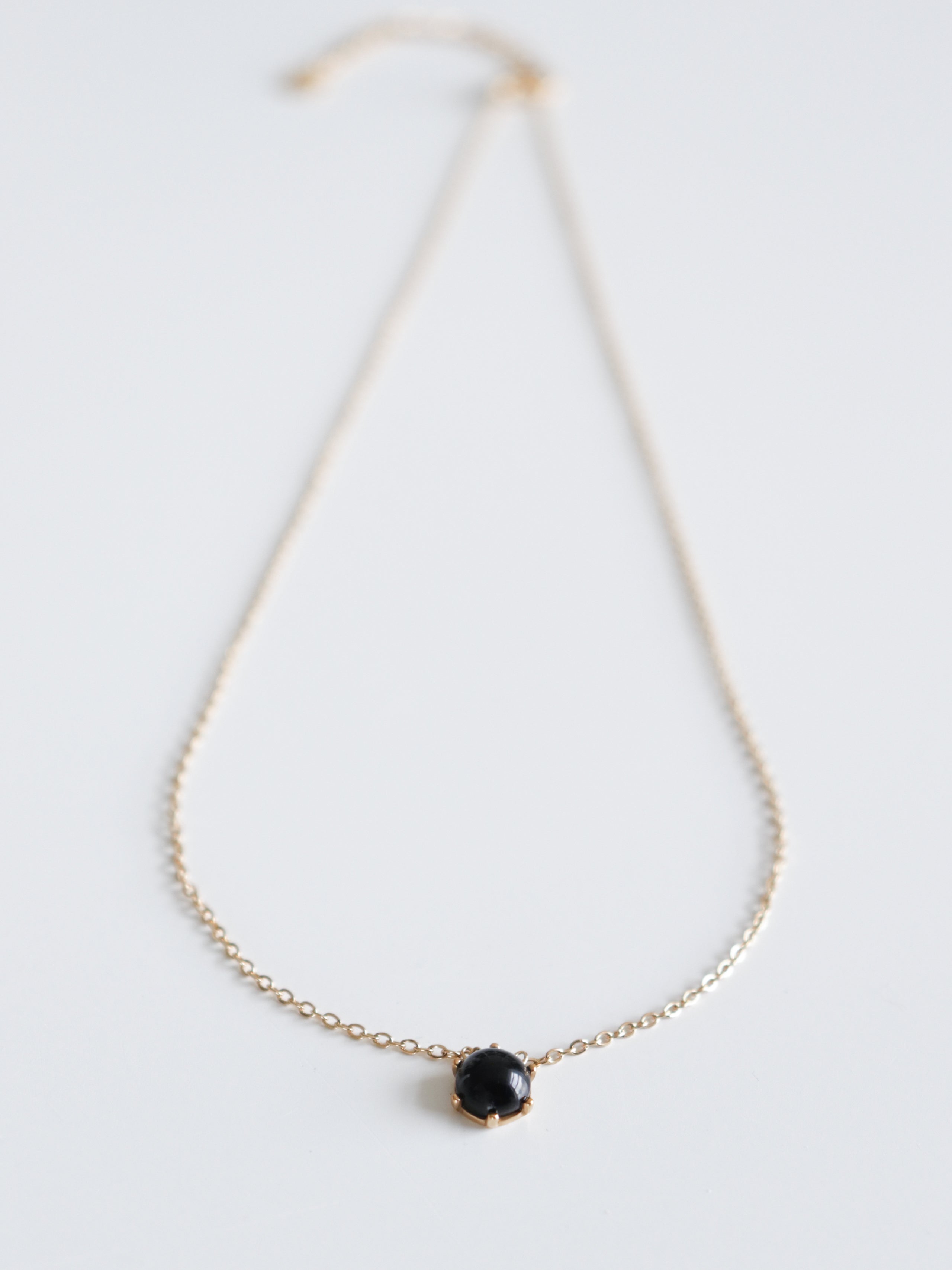 Kaklarota - Pusnakts by Como Jewelry ir maiga juveliertērauda kaklarota ar mazu, apaļu melnu dārgakmens piekariņu uz balta fona.