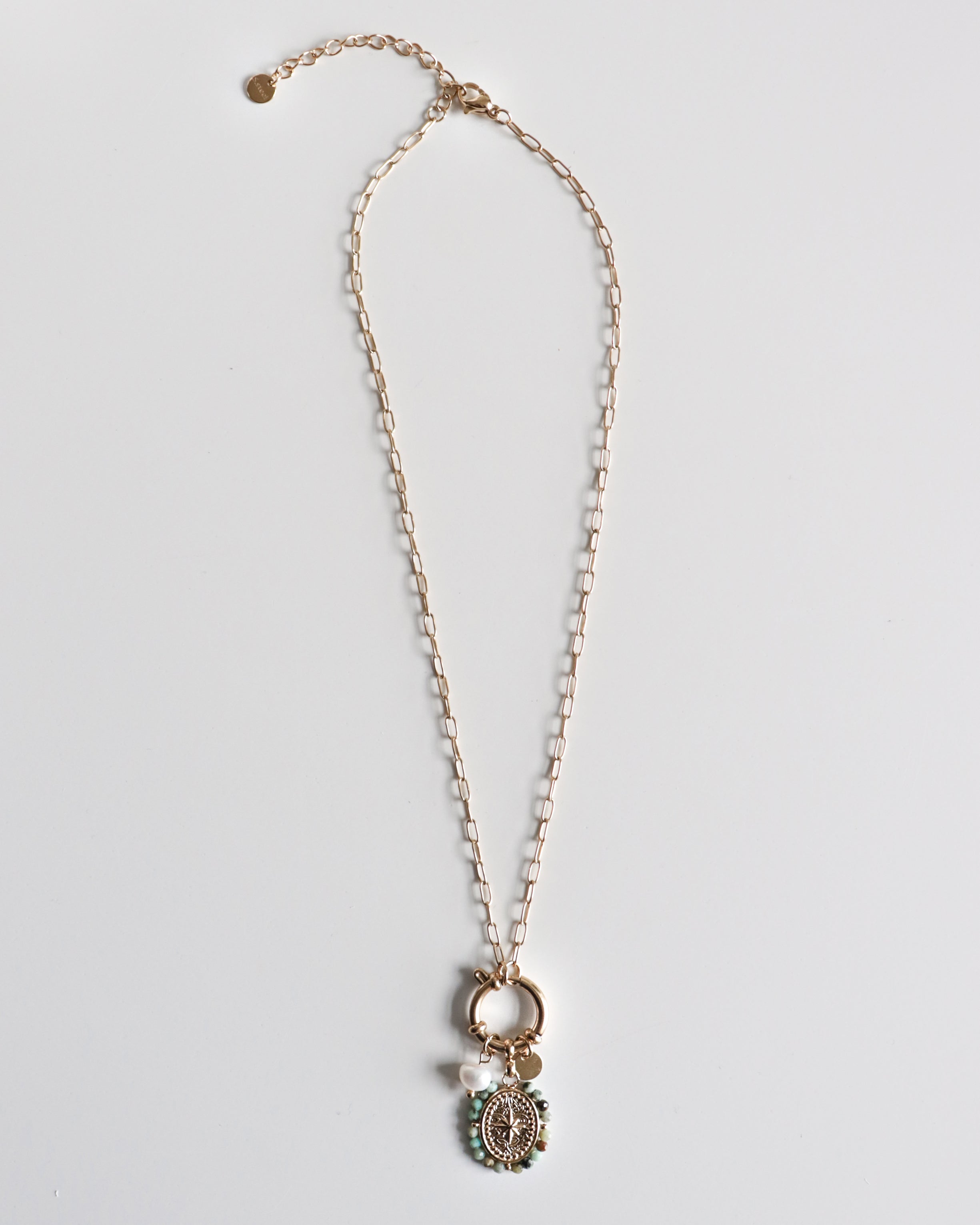 Como Jewelry Kaklarota - Vēja roze: antialerģiska zelta kaklarota sievietēm ar apaļu kulonu, dekorētu smalkām zaļām pērlītēm un detalizētu dizainu, eleganti noformēta uz balta fona. Ideāli piemērota ikdienai un svētkiem.