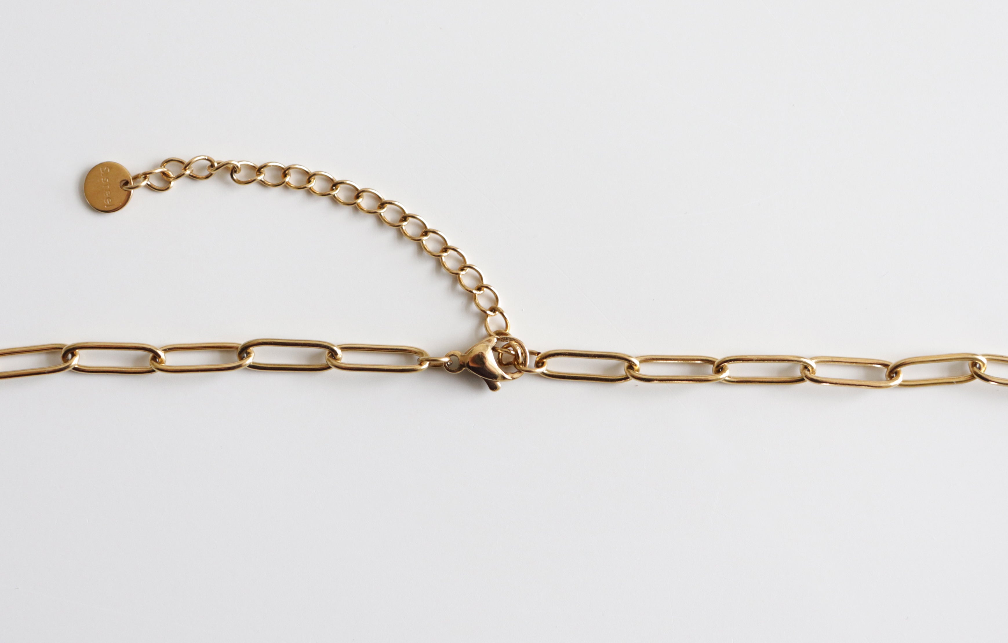 Kaklarota - Zaļās saules ceļš no Como Jewelry ir ar lielām taisnstūra formas saitēm un regulējamu pagarinājumu ar apaļu birku, kas to padara par stilīgu un izturīgu izvēli sievietēm, un tas ir uz balta fona.