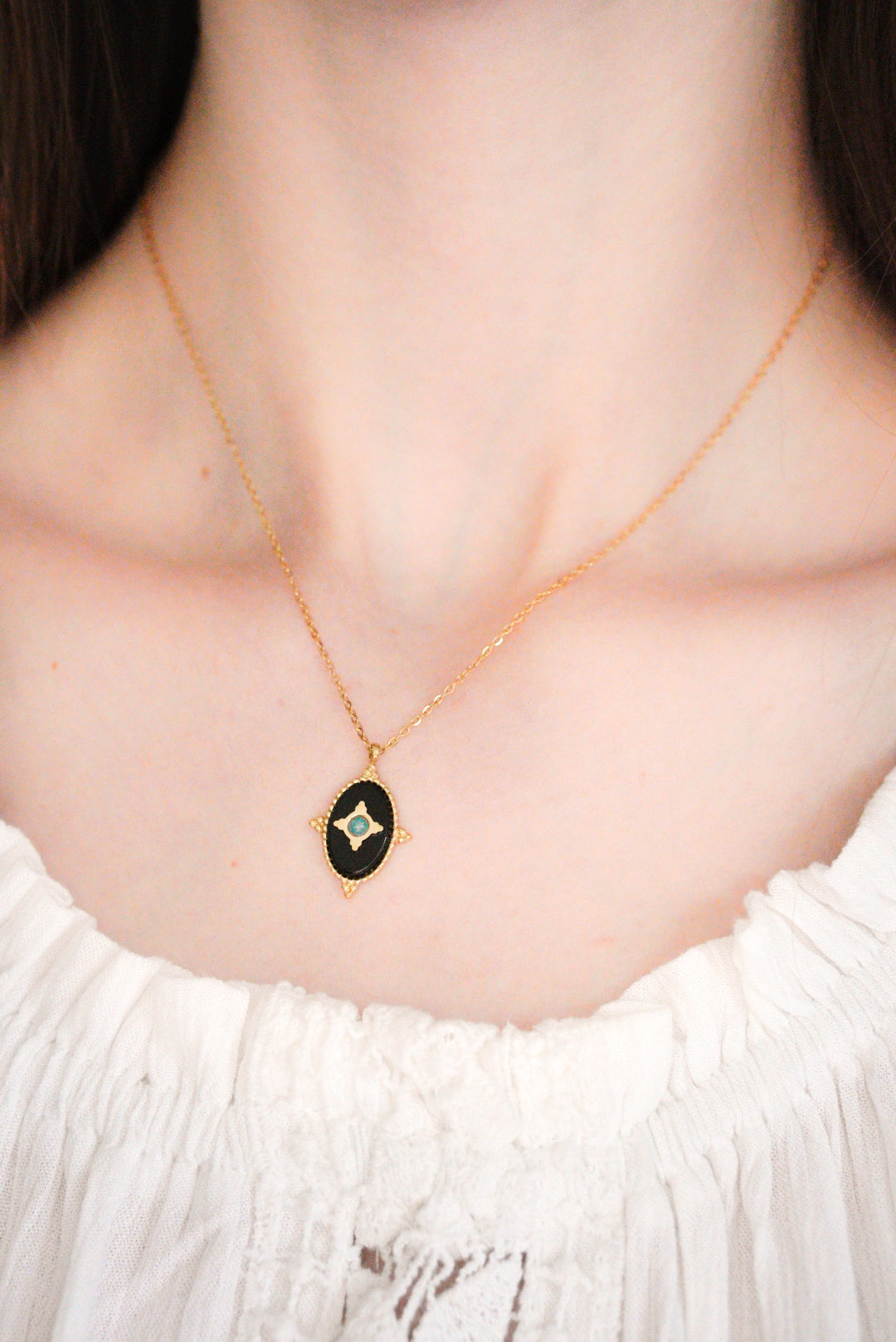 Sieviete valkā baltu blūzi ar Como Jewelry "Kaklarota - Pusnakts talismans" - modernu kaklarotu ar melnu ovālu piekariņu un centrālo dārgakmeni, galveno uzmanību pievēršot viņas kaklam un šim elegantajam aksesuāram.