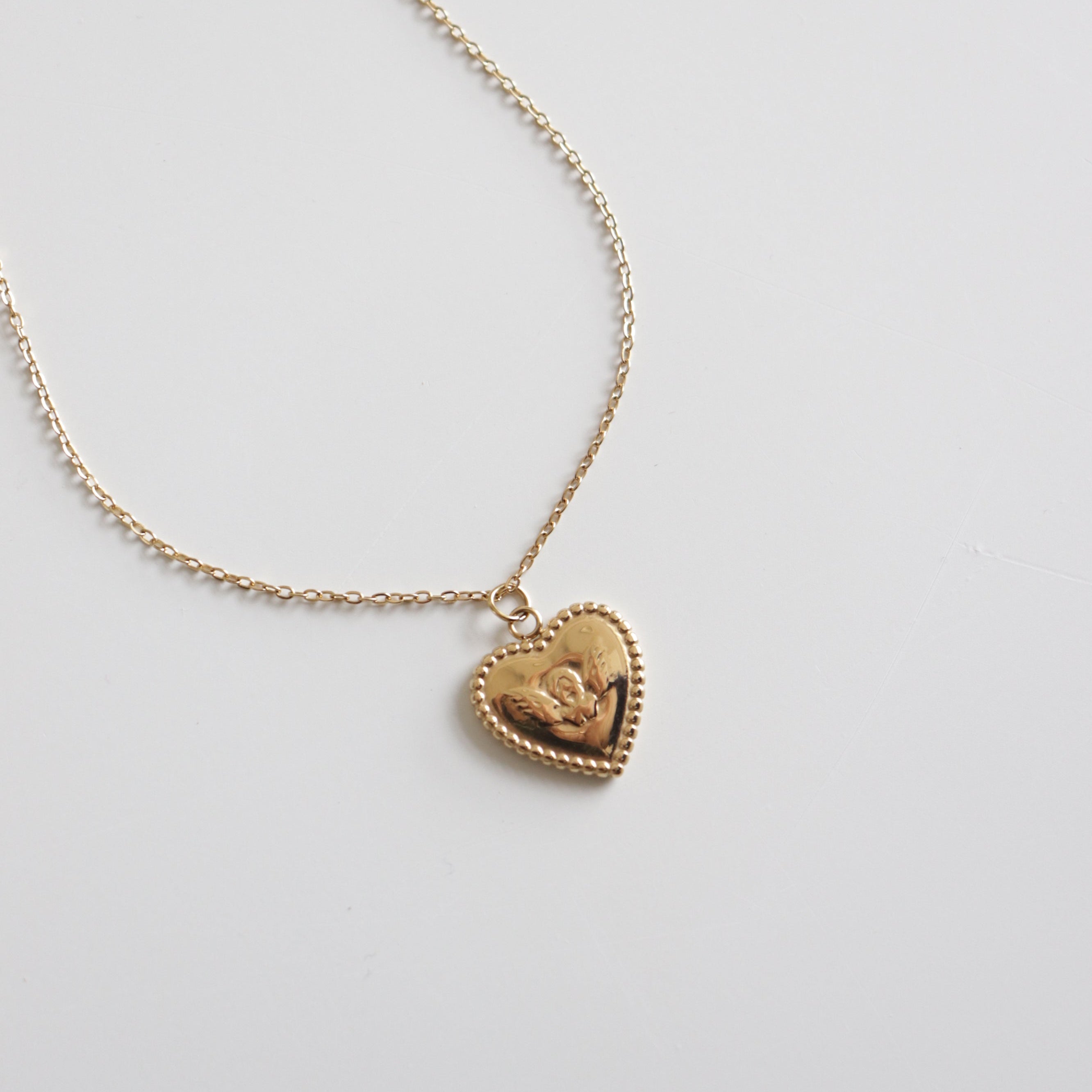 Kaklarota - Sirds by Como Jewelry ir maiga juveliertērauda kaklarota ar mazu, sirds formas piekariņu ar rožu dizainu, kas attēlots uz balta fona.