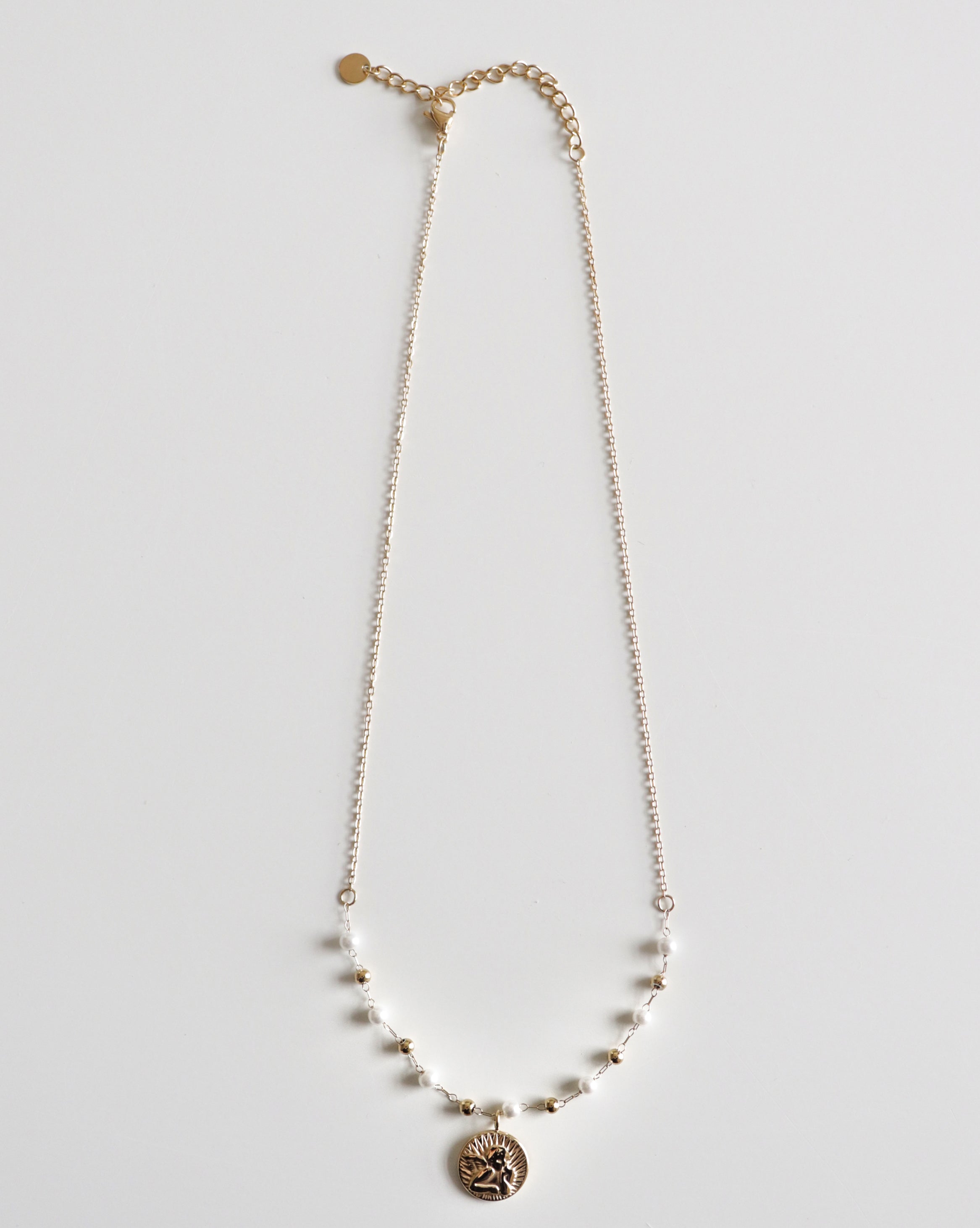 Mūsdienīga Kaklarota - Amors no Como Jewelry sievietēm ar mazām bumbiņām un apaļu gravētu saulespuķes kulonu, izcelta uz balta fona.