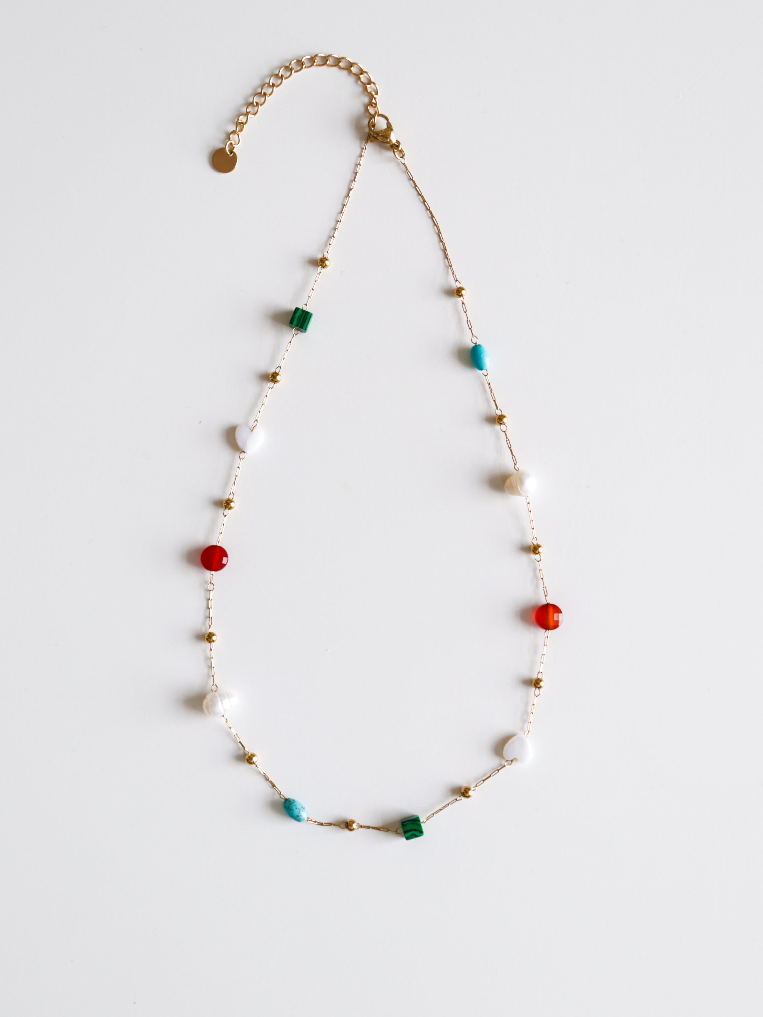 Kaklarota - Krāsu rotaļa no Como Jewelry ir smalka zelta ķēdīte ar mazām zelta, baltām, sarkanām, zaļām un tirkīza pērlītēm uz balta fona.