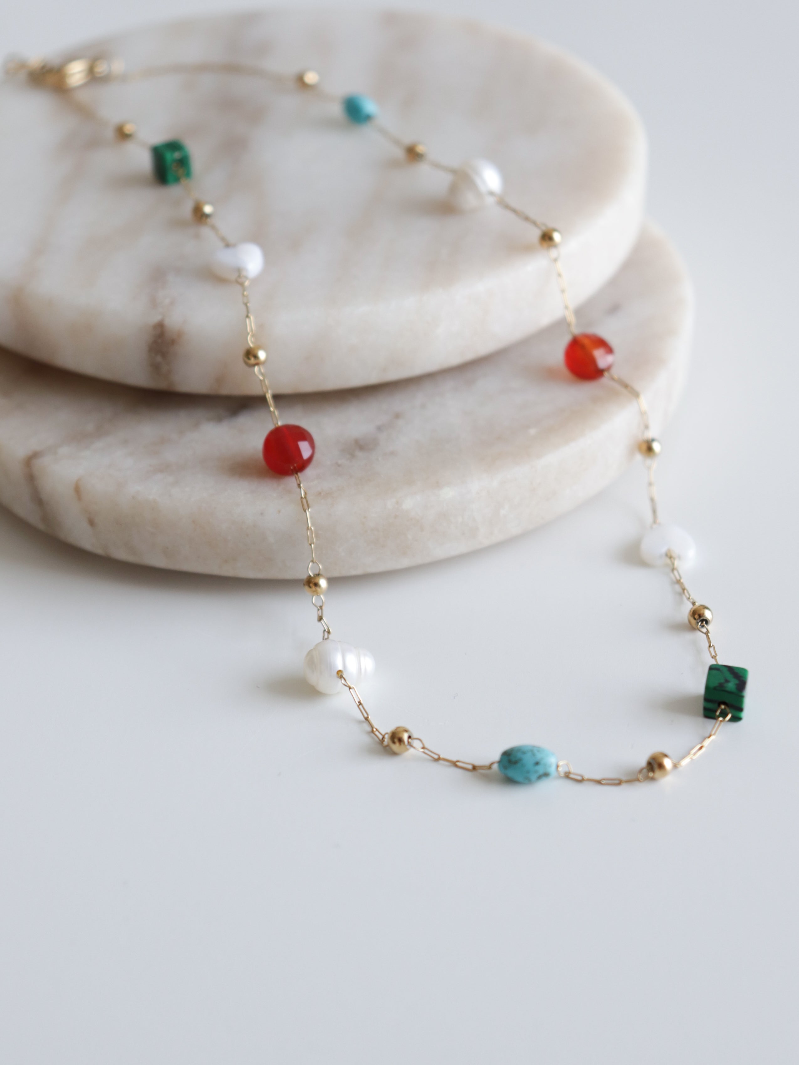 Como Jewelry Kaklarota - Krāsu rotaļa ir mūsdienīga kaklarota sievietēm ar rotaļīgu sarkanu, zaļu, tirkīza un baltu pērlīšu rakstu. Eleganti izvietota uz divām apaļām marmora plāksnēm.