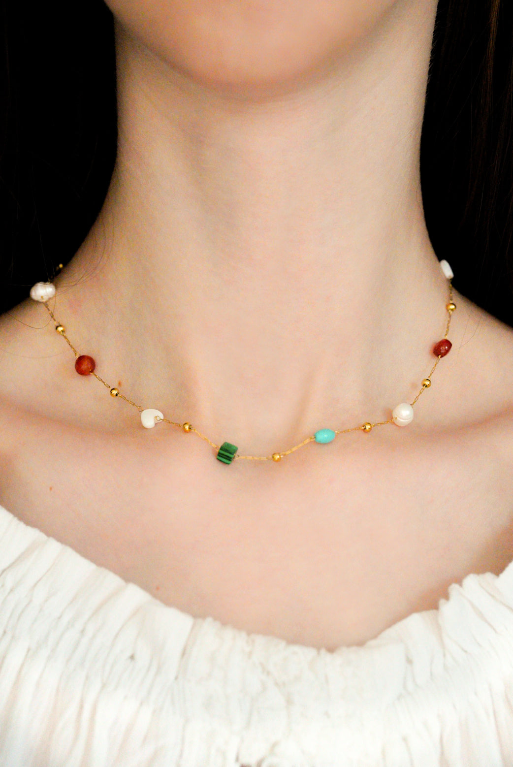 Sievietes kakla tuvplāns, uz kura valkā Como Jewelry Kaklarota - Krāsu rotaļa, antialerģiska rotaslieta ar mazām, krāsainām pērlītēm un pērlītēm, kas kombinēta ar baltas krāsas tekstūras topu bez pleciem. Stilīgs un maigs ādai.