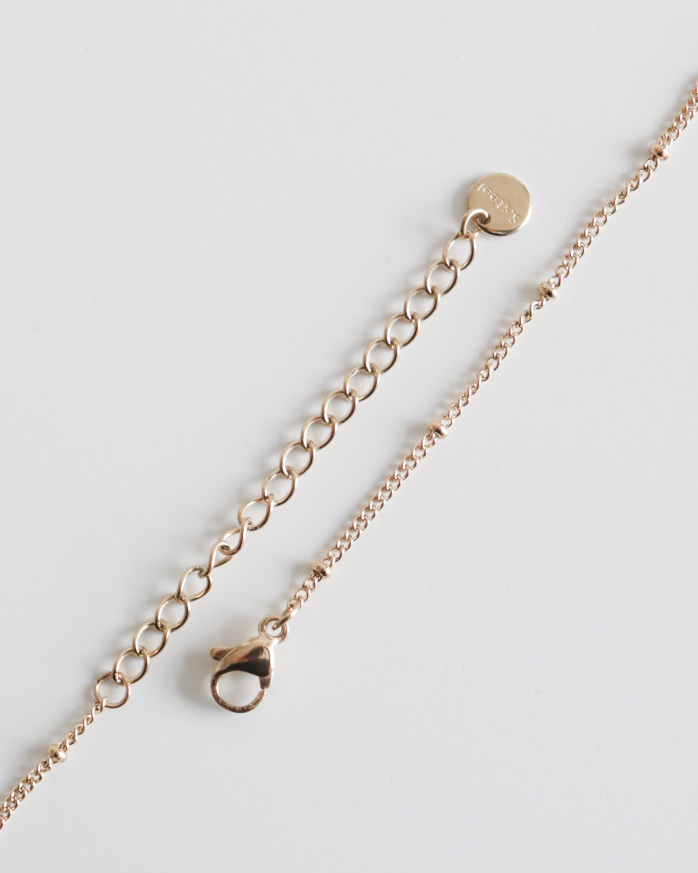 Como Jewelry "Kaklarota - Sirds" kaklarota ar omāra aizdari, regulējamu pagarinātāju un mazu apaļu birku uz balta fona. Šī antialerģiska rotaslieta ir stilīga un ērta valkāšanai ikdienā.