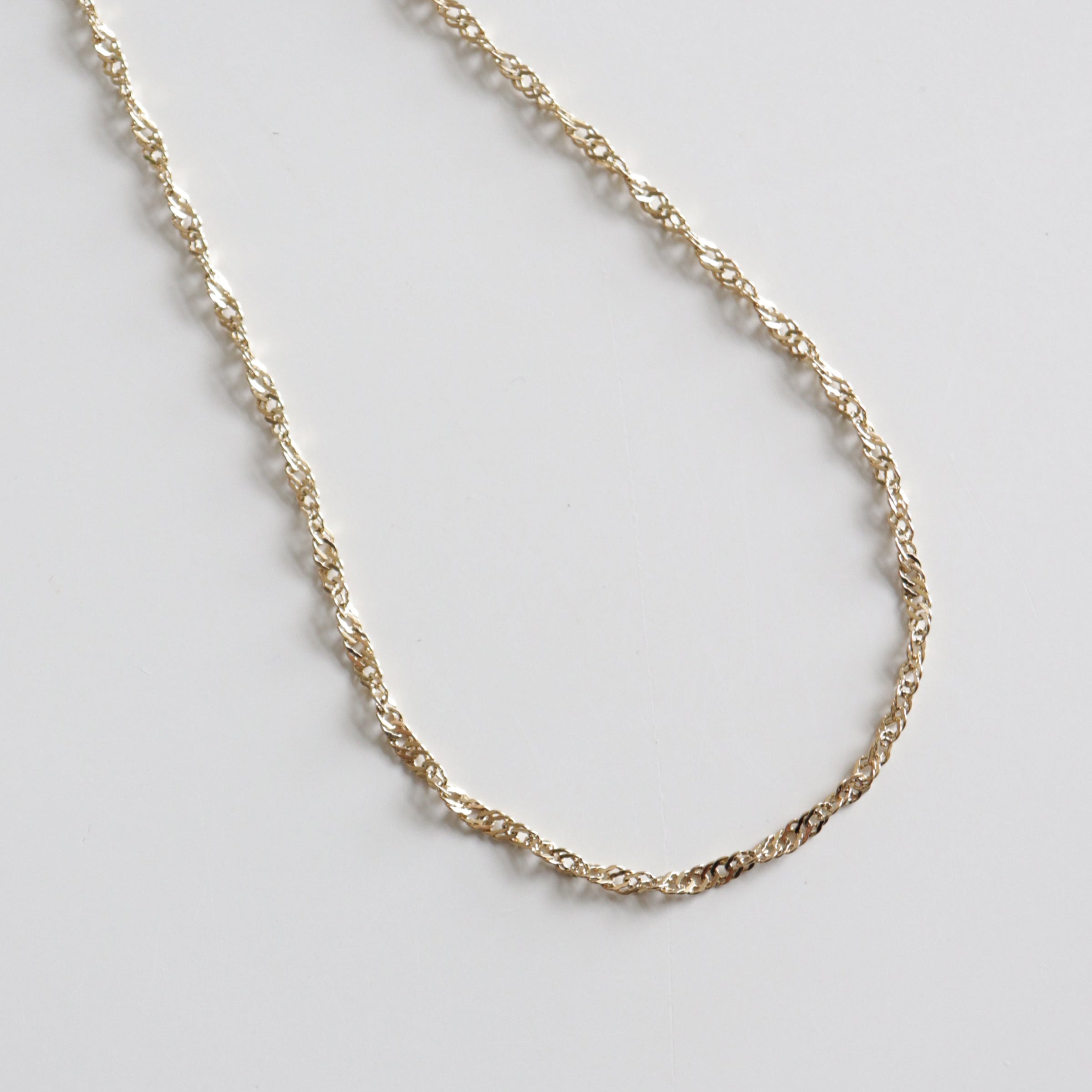 Kaklarota - Zelta vijums no Como Jewelry ir maiga zelta kaklarota ar vītu virves ķēdīti, kas ovālas formas ovālā formā izvietota uz balta fona.