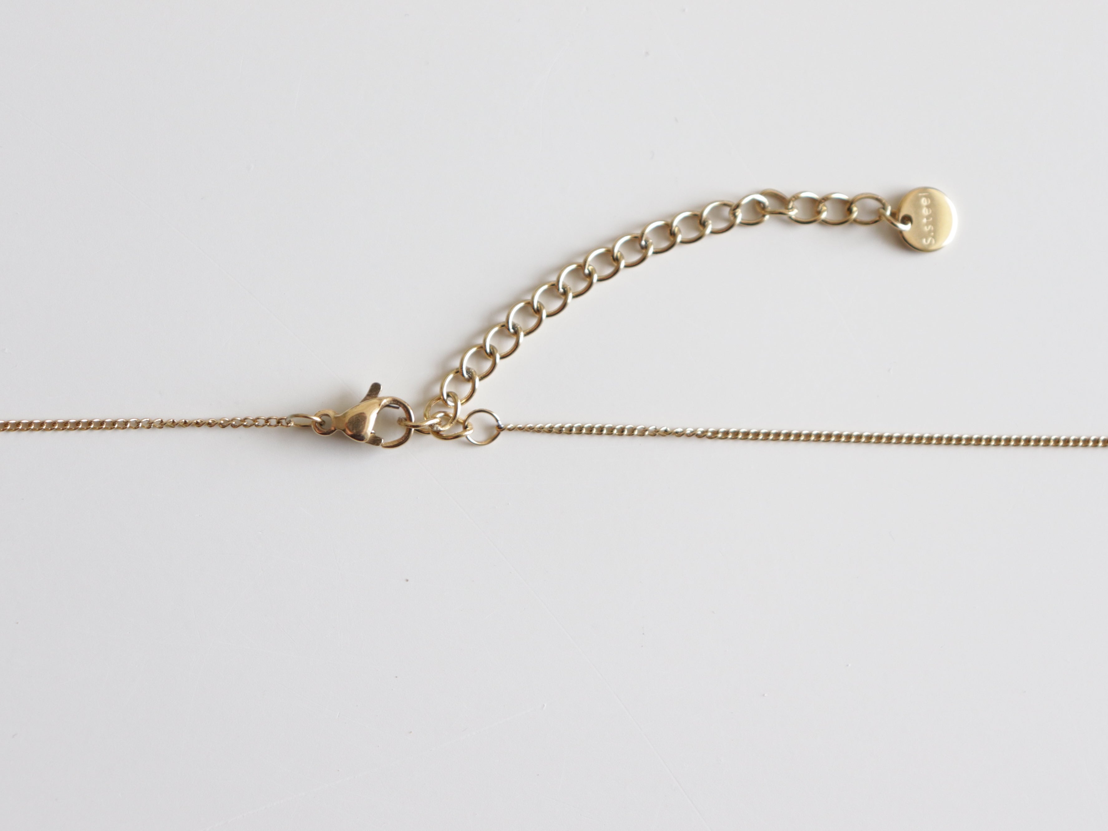 Kaklarota - Rio by Como Jewelry ir aprīkota ar slaidu ķēdīti, omāra aizdares aizdari un regulējamu pagarinājumu ar nelielu apaļu birku, kas izceļas uz balta fona.