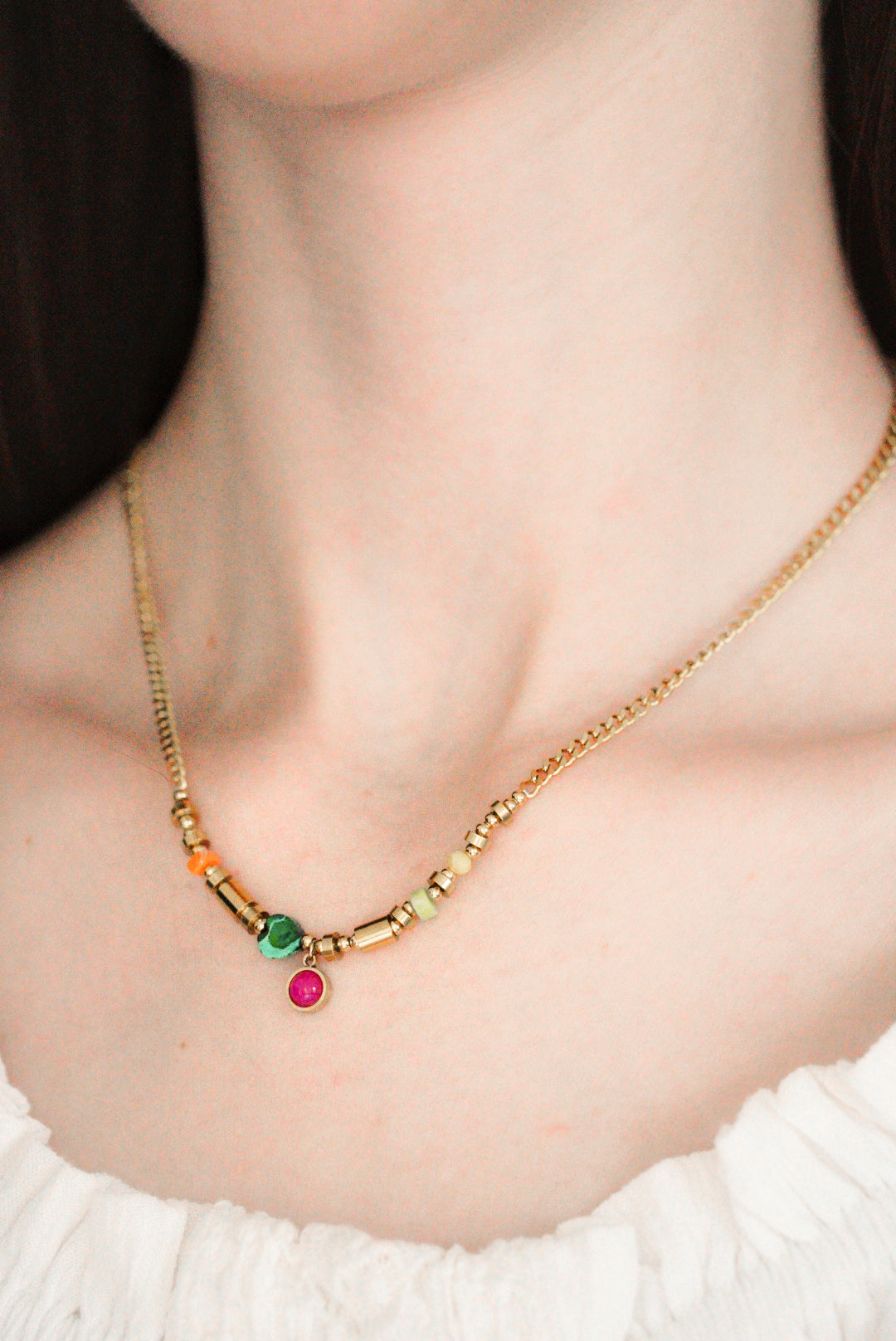 Tuvplāns sievietes kaklam, kurai uz kakla ir Como Jewelry Kaklarota - Rio - antialerģiska kaklarota ar krāsainām pērlītēm un maziem piekariņiem ar zaļiem, rozā un oranžiem akmentiņiem, kas kombinēta ar baltu faktūru.