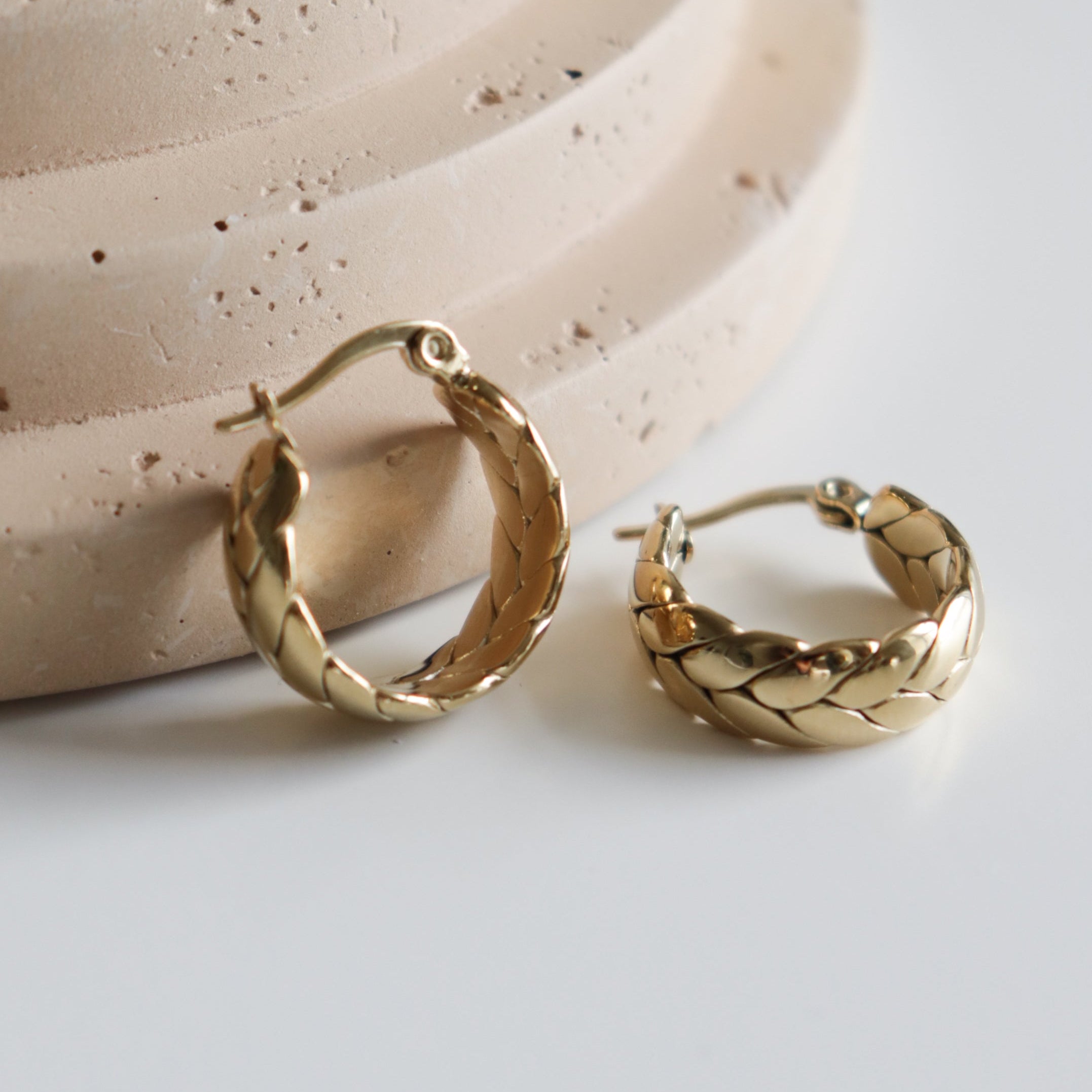 Como Jewelry Mazie auskari - Vijums pīti riņķveida auskari, ideāli piemēroti jutīgai ādai, izvietoti uz gludas, gaiši smilškrāsas faktūras virsmas.