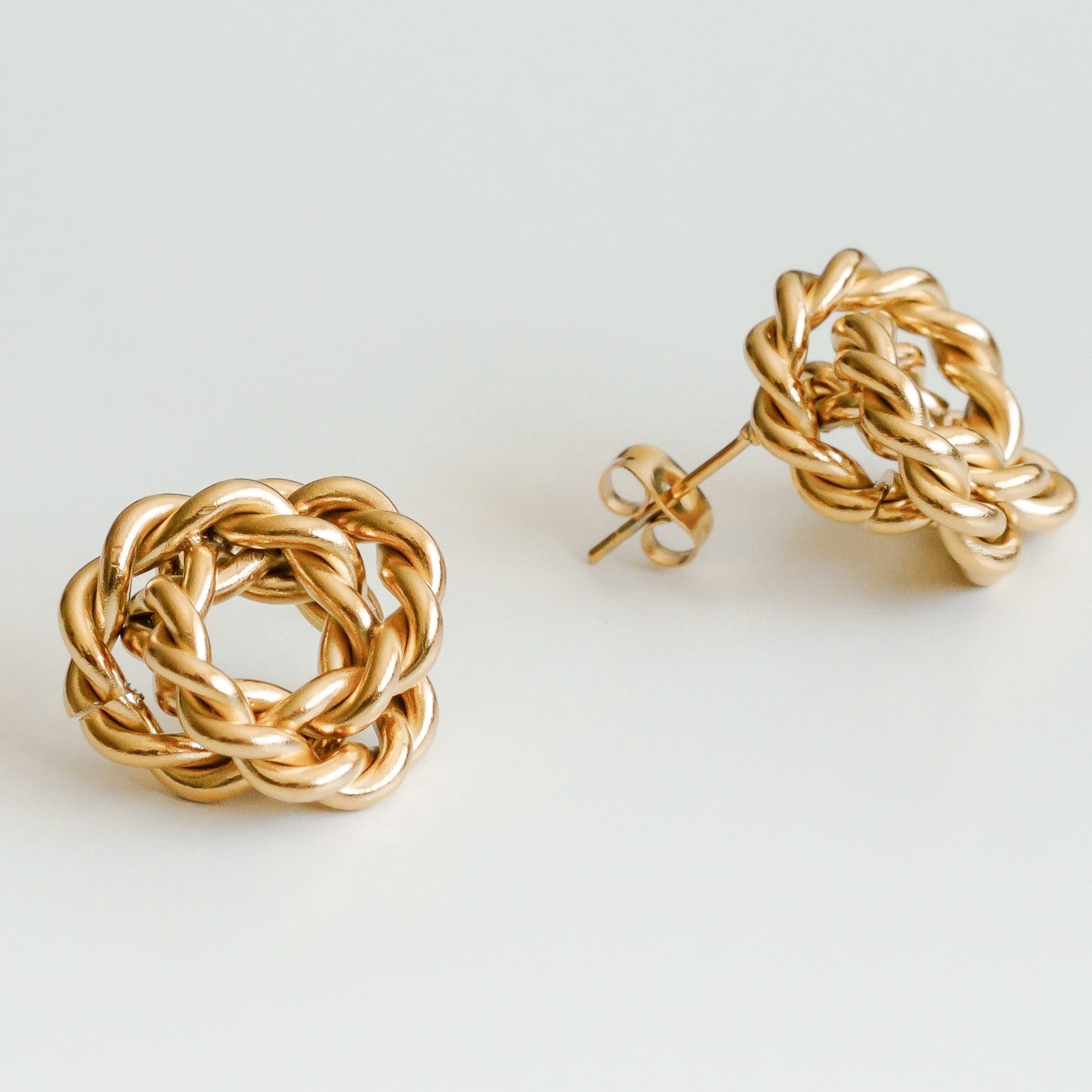 Como Jewelry "Mazie auskari - Mezgls" ir zelta mezglu auskari ar sarežģītu pītu dizainu, ko iedvesmojis Nameja auskariņi un kas attēlots uz baltas virsmas.