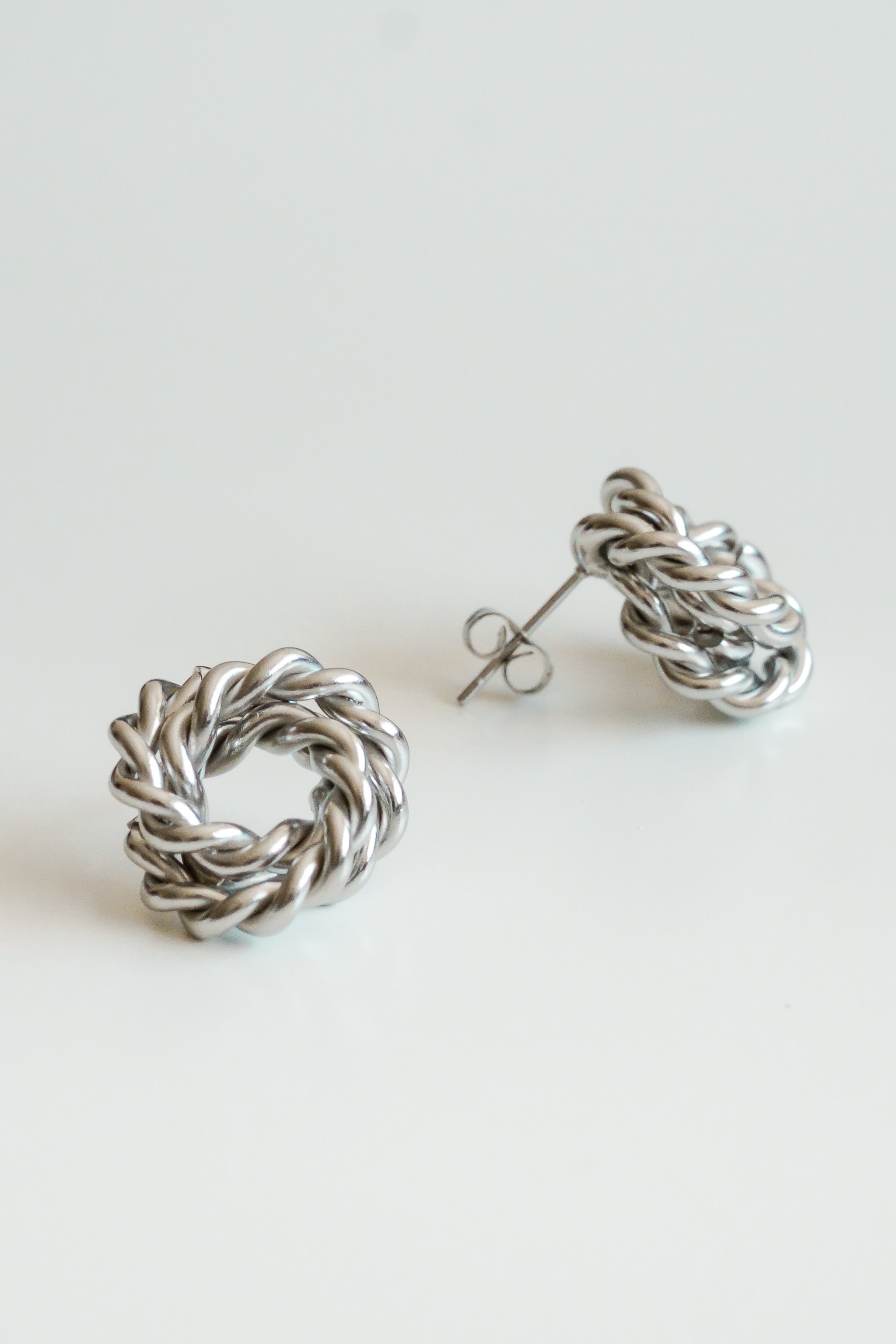 Divas Mazie auskari - Mezgls by Como Jewelry sudraba piespraudes ar savītu, pītu apļveida dizainu ir attēlotas uz balta fona - viena ir plakana, bet otra ir atbalstīta, lai redzētu stieni un tauriņa pamatni.