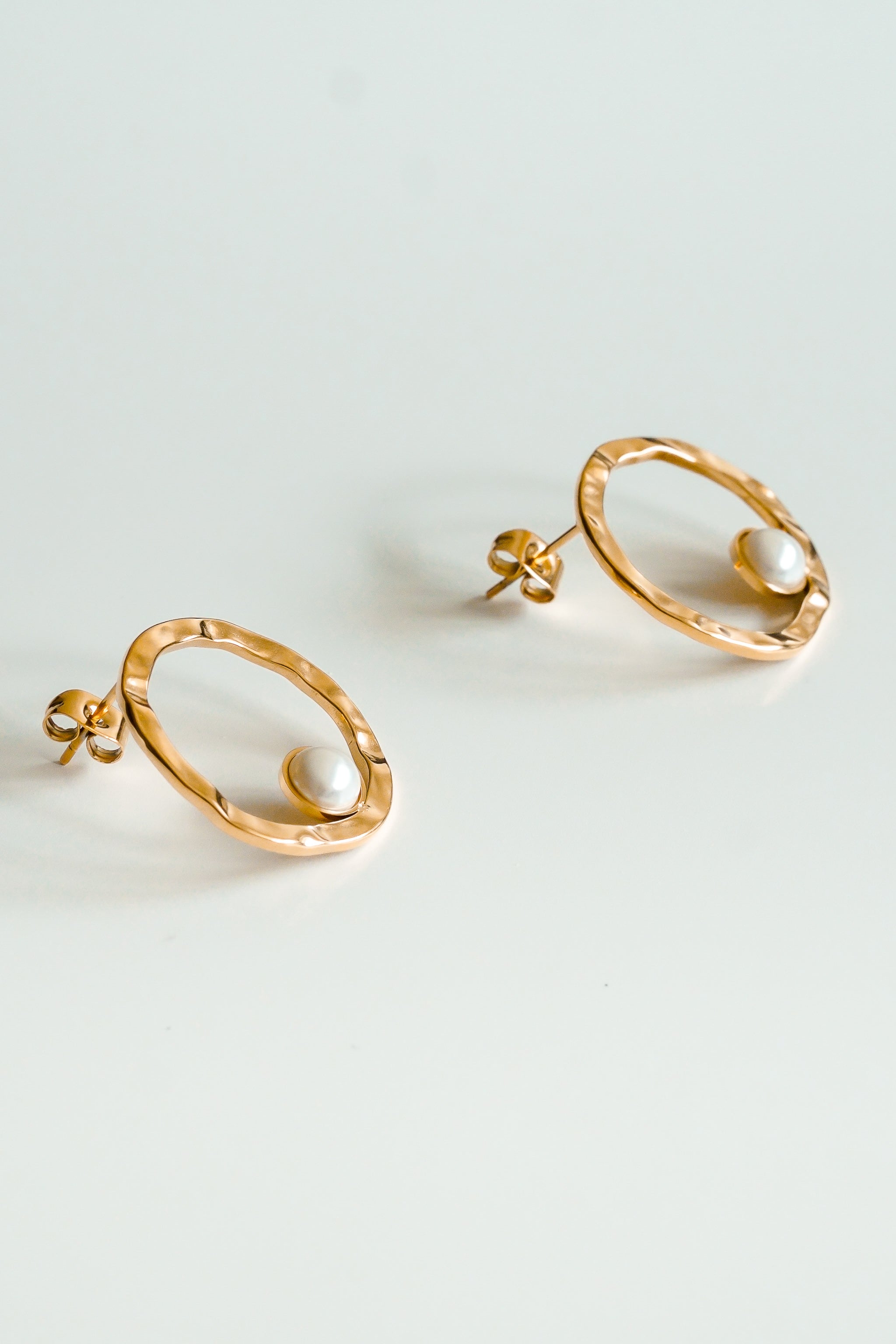 Como Jewelry Mazie auskari - Rietošā pērle ir ar neregulārām ovālām zeltītām ovālām cilpiņām, no kurām katru rotā viena balta pērle pie pamatnes, kas piešķir modernu eleganci, un tās ir uz balta fona.