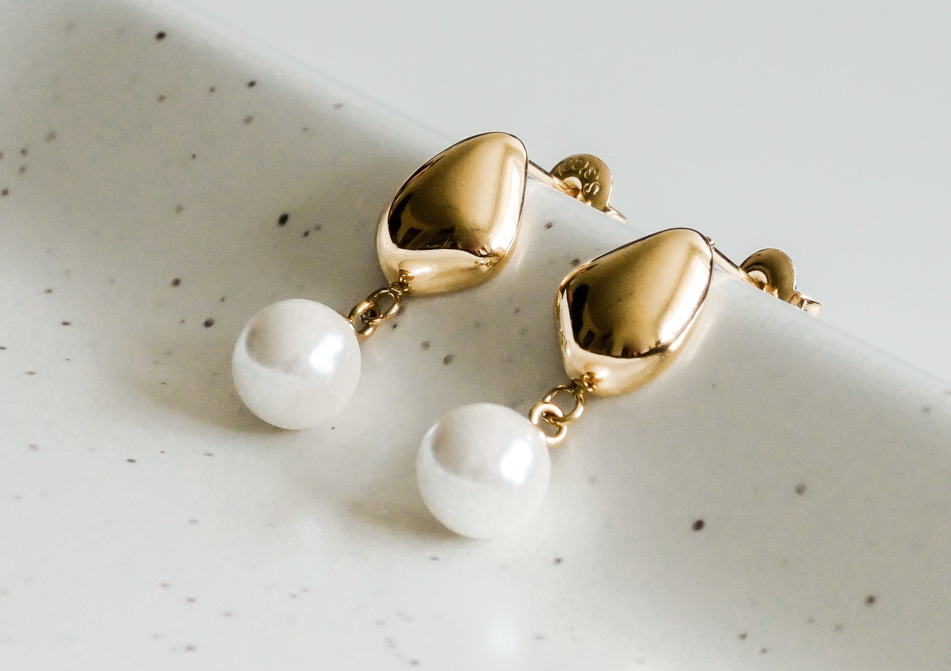 Mazie auskari - Rīta rasa no Como Jewelry ar spīdīgām asaru galotnēm un apaļām baltām pērlēm līdzīgām pērlītēm, kas izvietotas uz raibas, baltas keramikas trauciņa - šie elegantie auskari piešķir mūžīgu šarmu jebkuram tēlam.