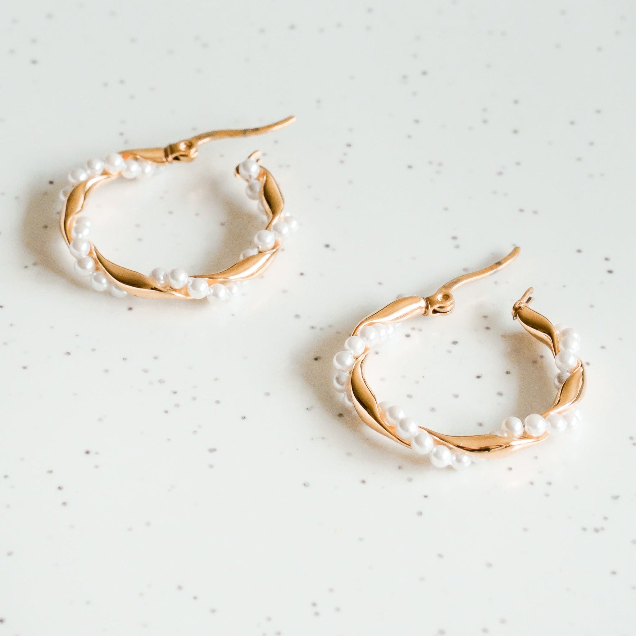 Mazie auskari - Pērļu vainags no Como Jewelry ar zelta pārklājumu uz nerūsējošā tērauda un baltām pērļu pērlītēm rada elegantu akcentu uz balta, viegli raibota fona.