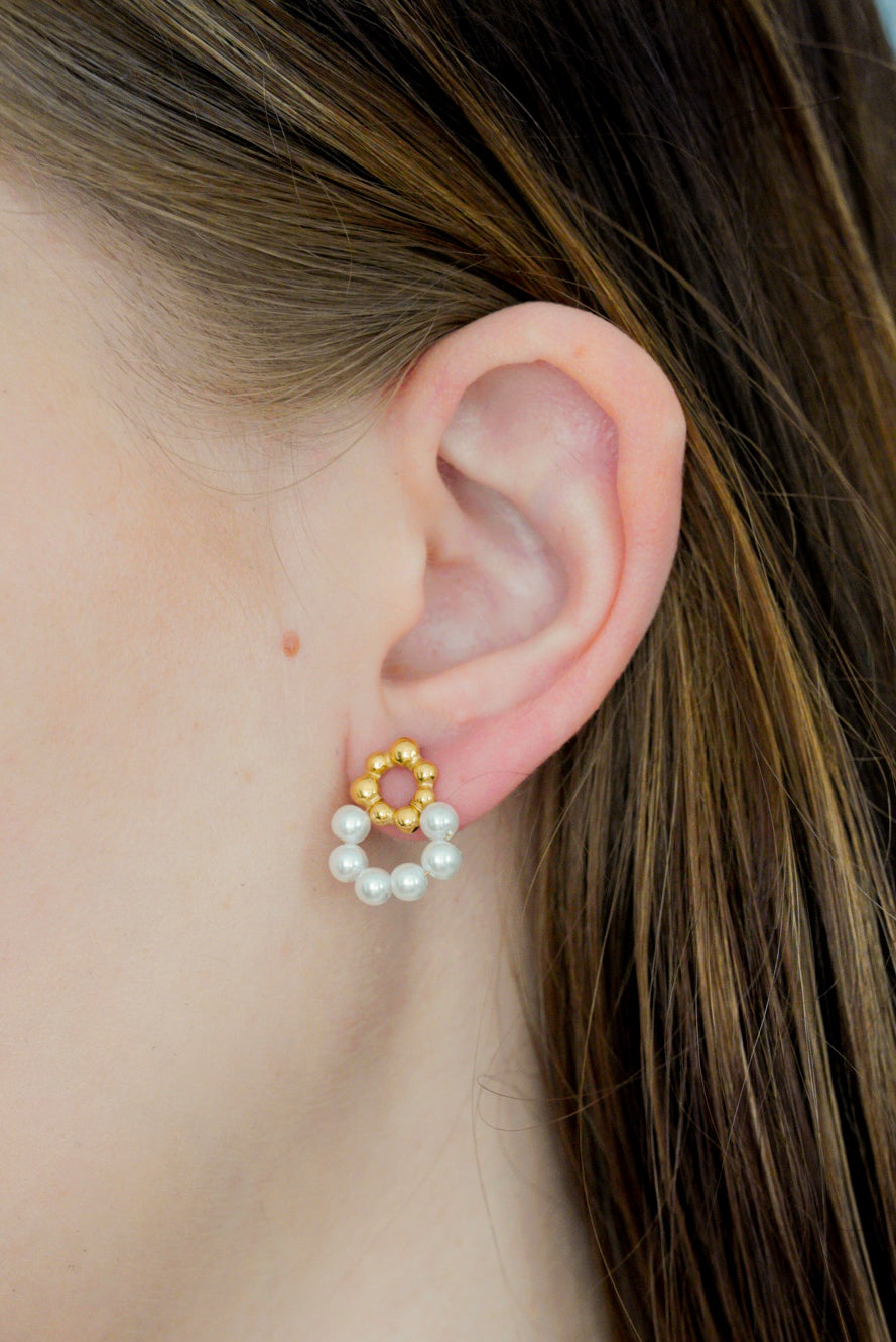 Tuvplāns personai ar gaišu ādu un taisniem brūniem matiem, kurai ir Como Jewelry Mazie auskari - Pērļu ziediņi: zelta ziedu zelta pārklāts nerūsējošais tērauds, akcentēts ar nelielu baltu pērļu pusapli.