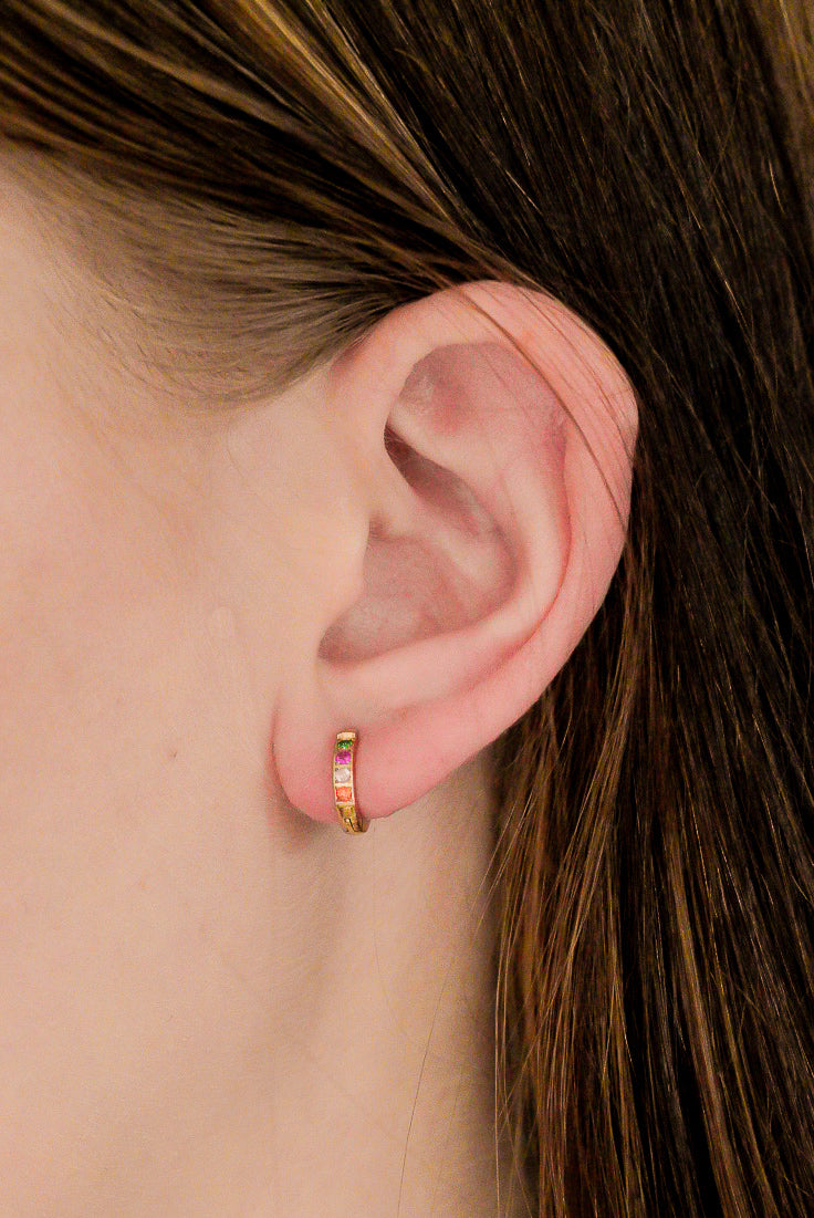 Tuvplāns personai ar gaišu ādu un taisniem, brūniem matiem, kurai ir Como Jewelry Mazie auskari - Krāsainie kristāli, mazas zelta cilpas ar daudzkrāsainiem kristāliem. Šie zelta pārklāta tērauda ūdensizturīgi auskari ir lieliski piemēroti ikdienas valkāšanai.