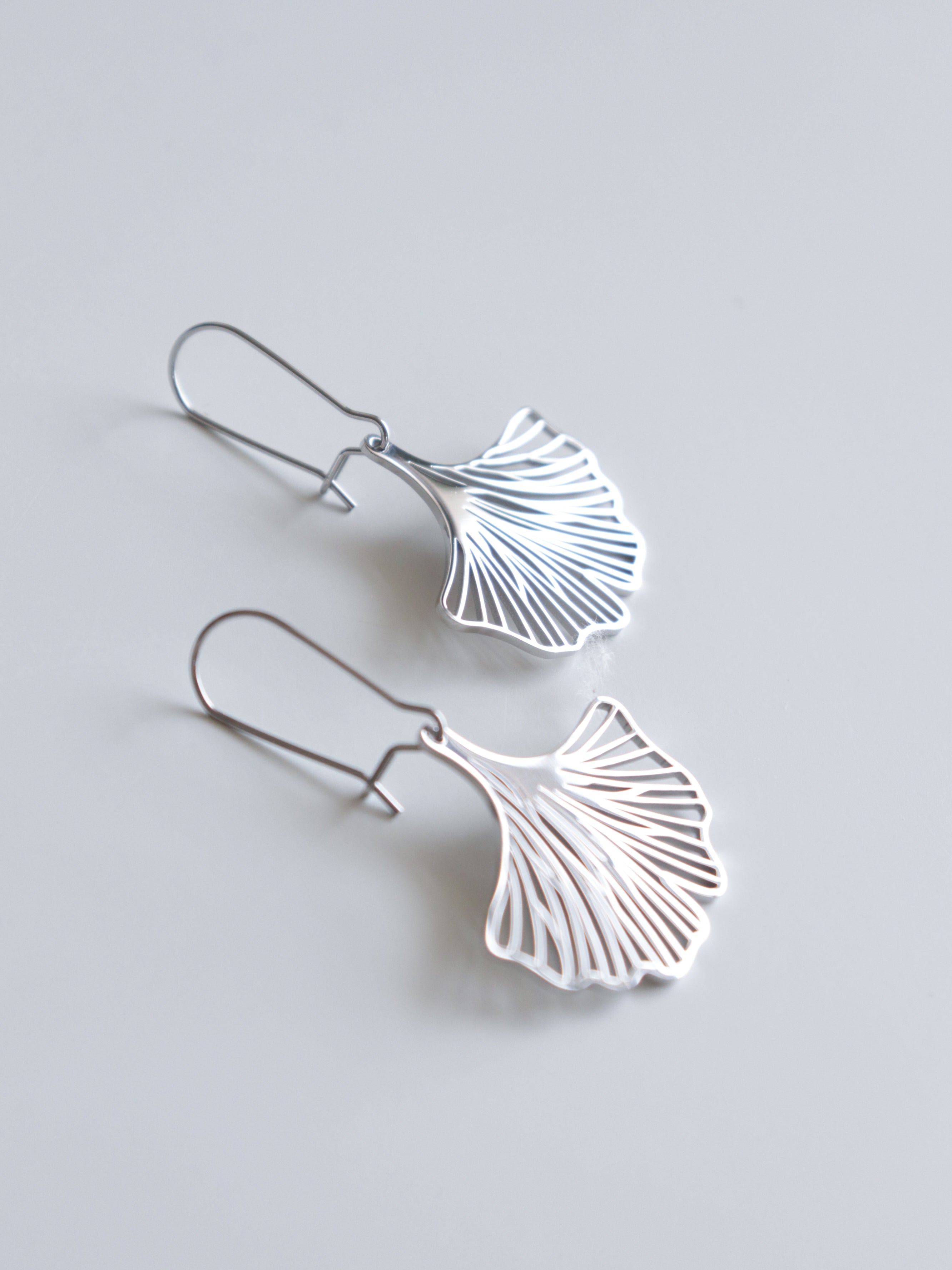 Como Jewelry Auskari - Ginkgo auskari ir ar maigām ginkgo lapu formām ar smalkām izgriezumu detaļām, kas skaisti izvietotas uz vienkārša gaiši pelēka fona.