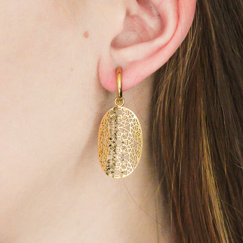 Tuvplāns personas ausij, kurai ir Como Jewelry Auskari - Aura: ovālas formas zelta auskari sievietēm ar teksturētu rakstu, kas karājas uz maza riņķīša. Personai ir gaiša āda un taisni gaiši brūni mati.