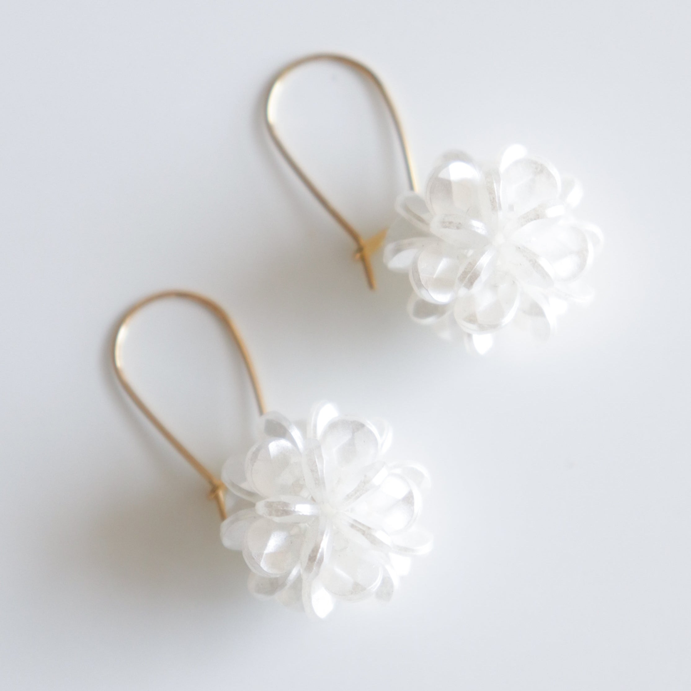 Como Jewelry Auskari - Rītausma: eleganta zelta auskari sievietēm ar maigiem, caurspīdīgi baltiem ziedu formas rotājumiem, demonstrēti uz neitrāla balta fona.