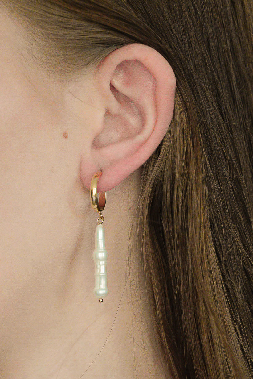 Tuvplāns uz personas auss ar taisniem brūniem matiem, kurai ir Como Jewelry Auskari - Lagūnas pērles-zelta loka auskari ar piekarināmu, neregulāras formas baltu pērļu pilienu.