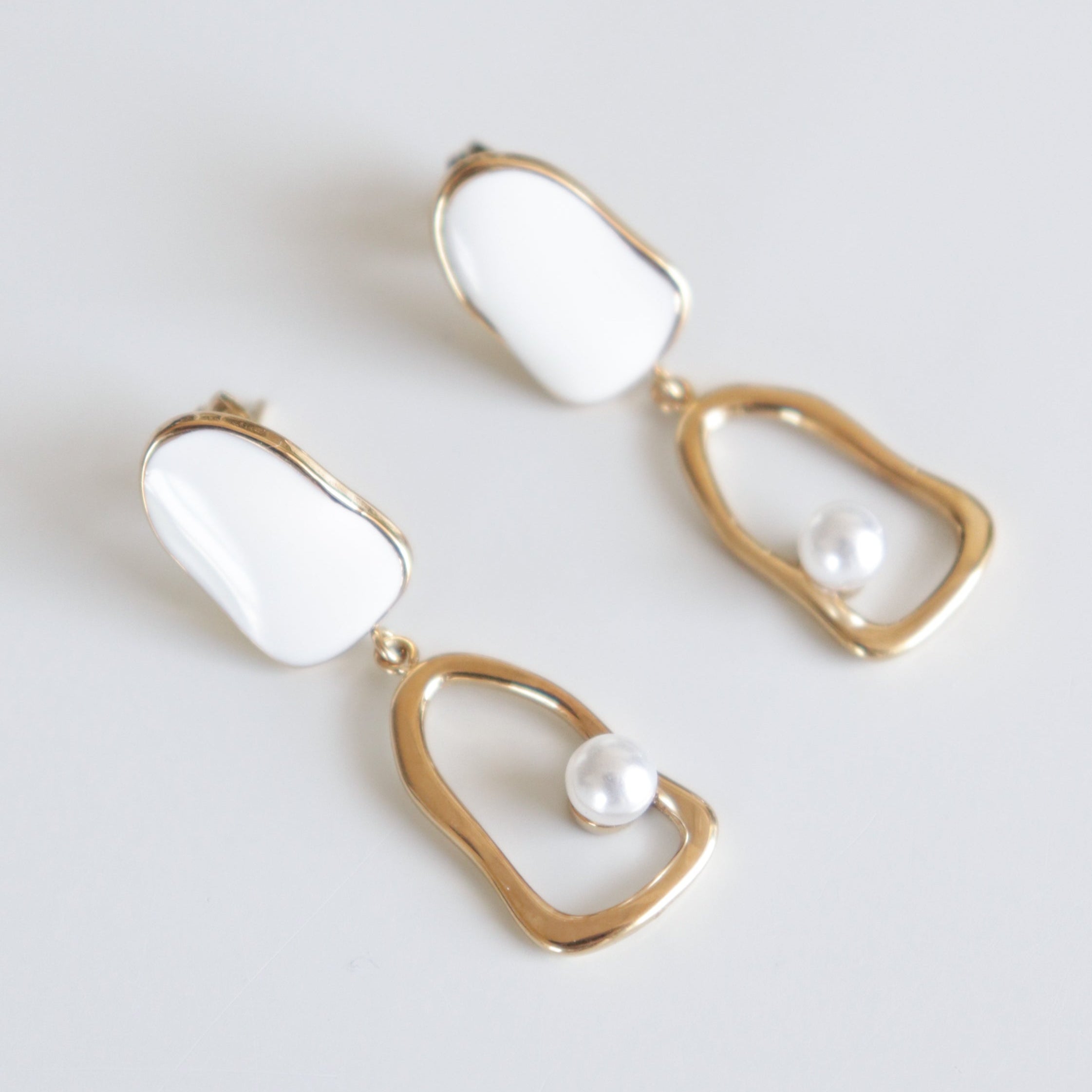 Como Jewelry Auskari - Atspulgs ir mūsdienīgi auskari ar neregulārām baltas emaljas virskārtas maliņām, atvērtiem zelta ietvariem un vienu pērļu pērlīti, kas iekarināta katrā auseklī. Ūdensizturīgi un ideāli piemēroti ikdienas elegancei.