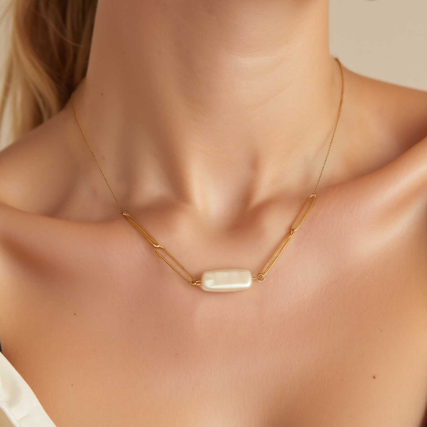 Sievietes tuvplāns, kurai mugurā ir Como Jewelry Kaklarota - Siltums kaklarota ar taisnstūra formas balto pērļu piekariņu. Viņa ir tērpusies baltā kreklā bez pleca un melnā siksniņā uz maigi izgaismota neitrāla fona.